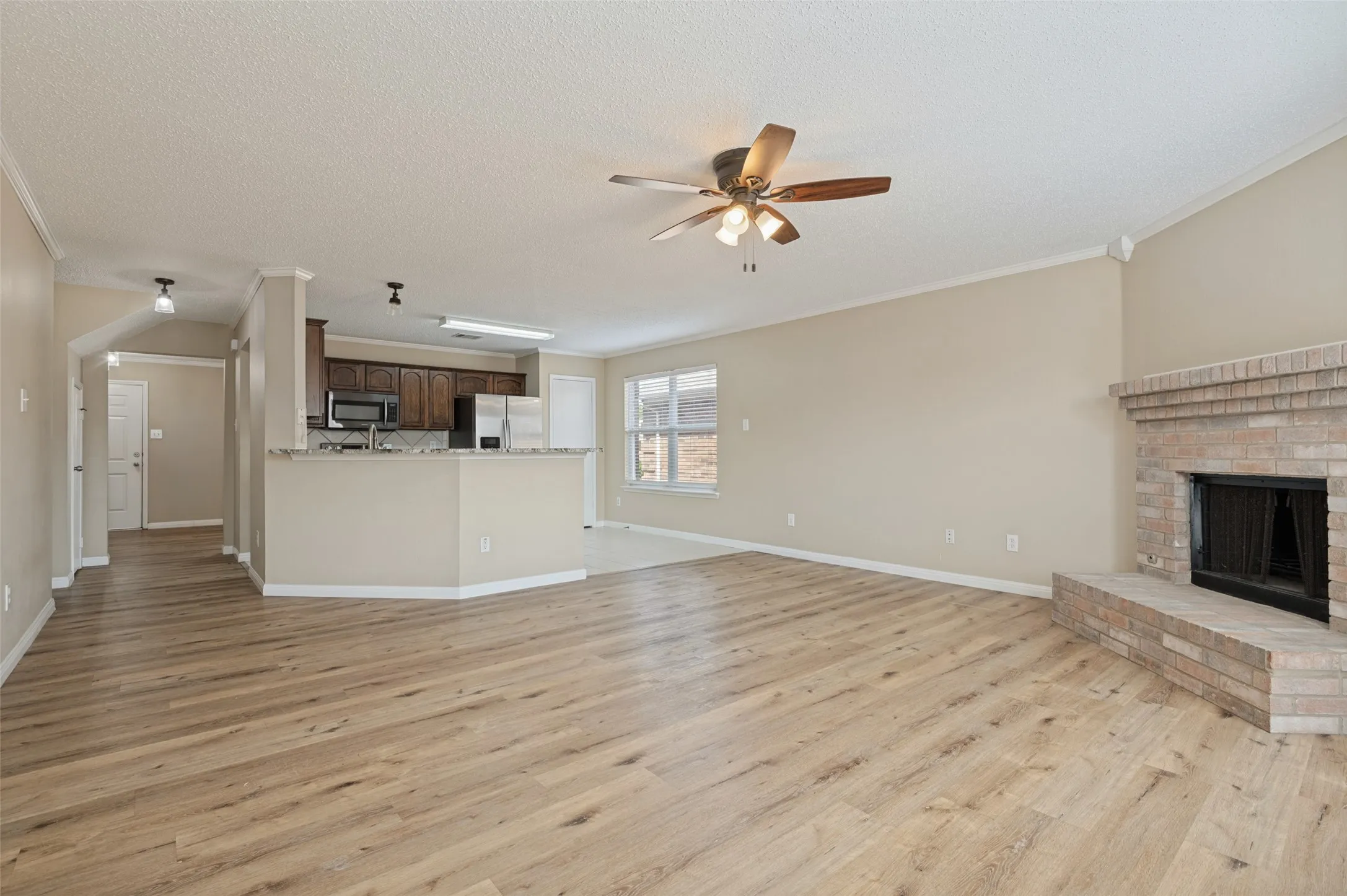Spacious living area featuring wood-finish flooring, a brick fireplace with hearth, and a ceiling fan