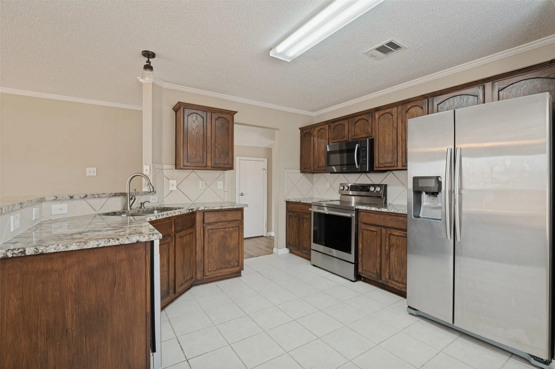 Kitchen featuring wood cabinetry, white tile flooring, stainless steel appliances, and light-toned countertops
