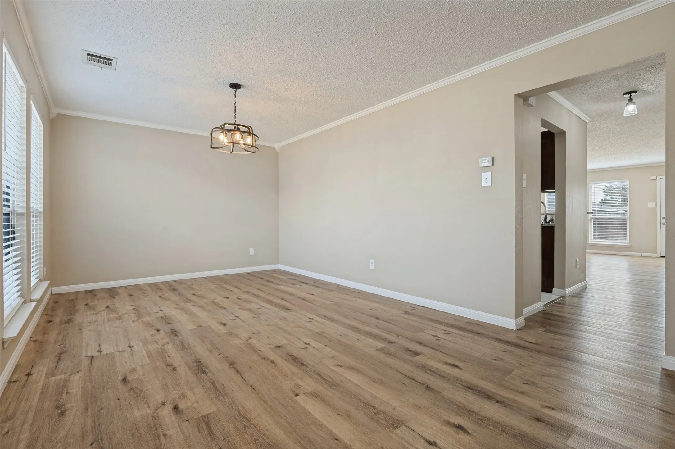 Wood-finish flooring, crown molding, modern light fixture, window blinds, and neutral wall tones