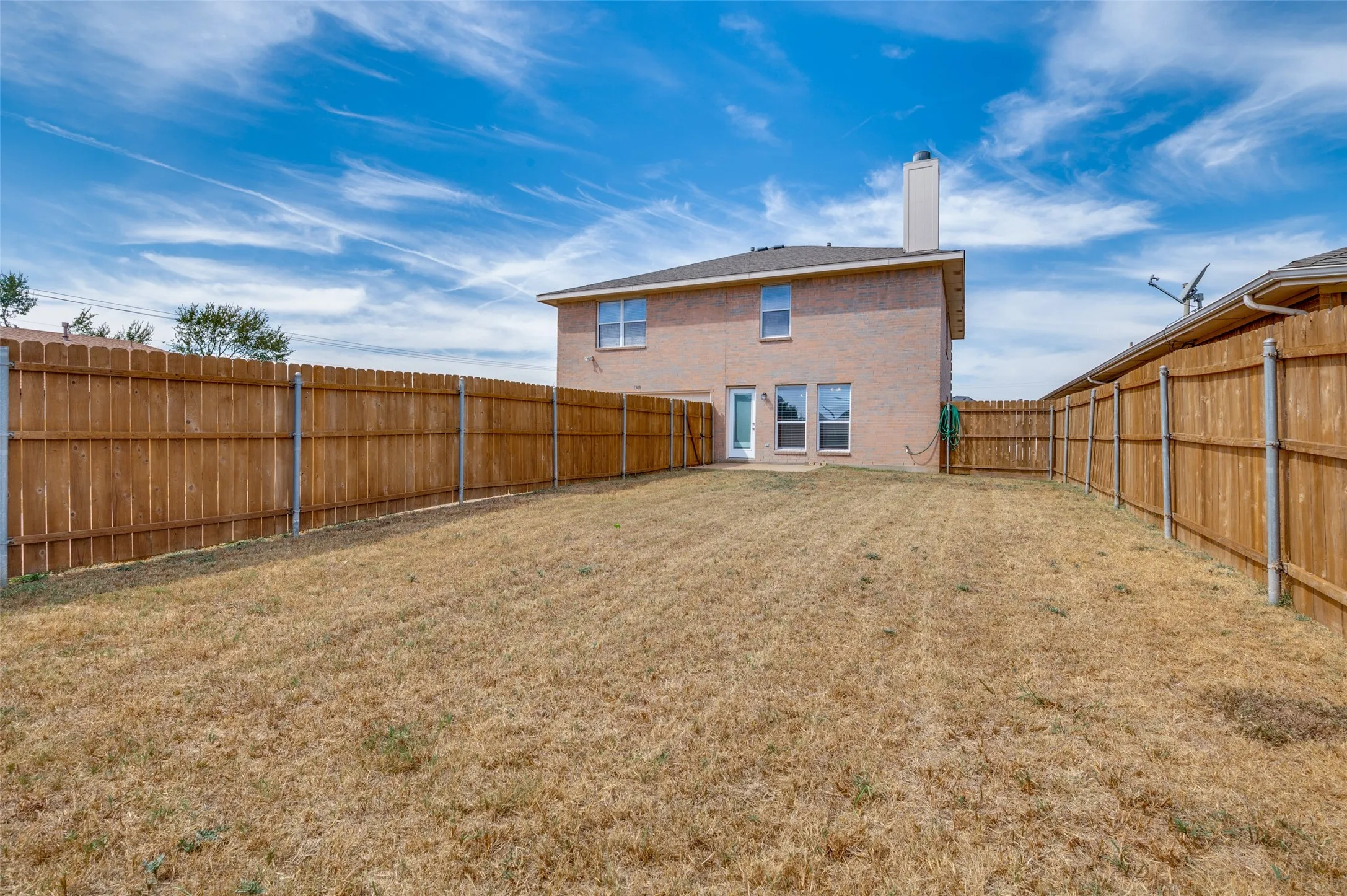 Expansive fenced backyard with brick exterior, multiple windows, and a prominent chimney