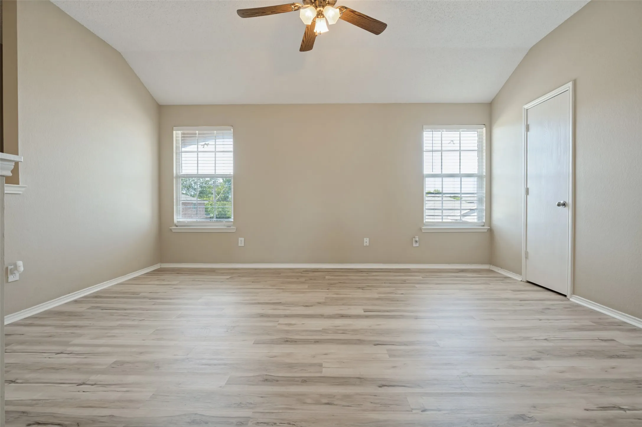 Vaulted ceiling with a ceiling fan, two windows, wood-finish flooring, and light-colored walls