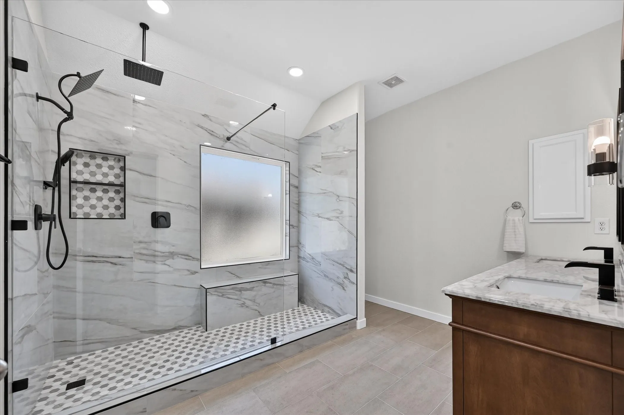 Walk-in shower with clear glass enclosure, marble-look tile walls, dual shower heads, and built-in bench