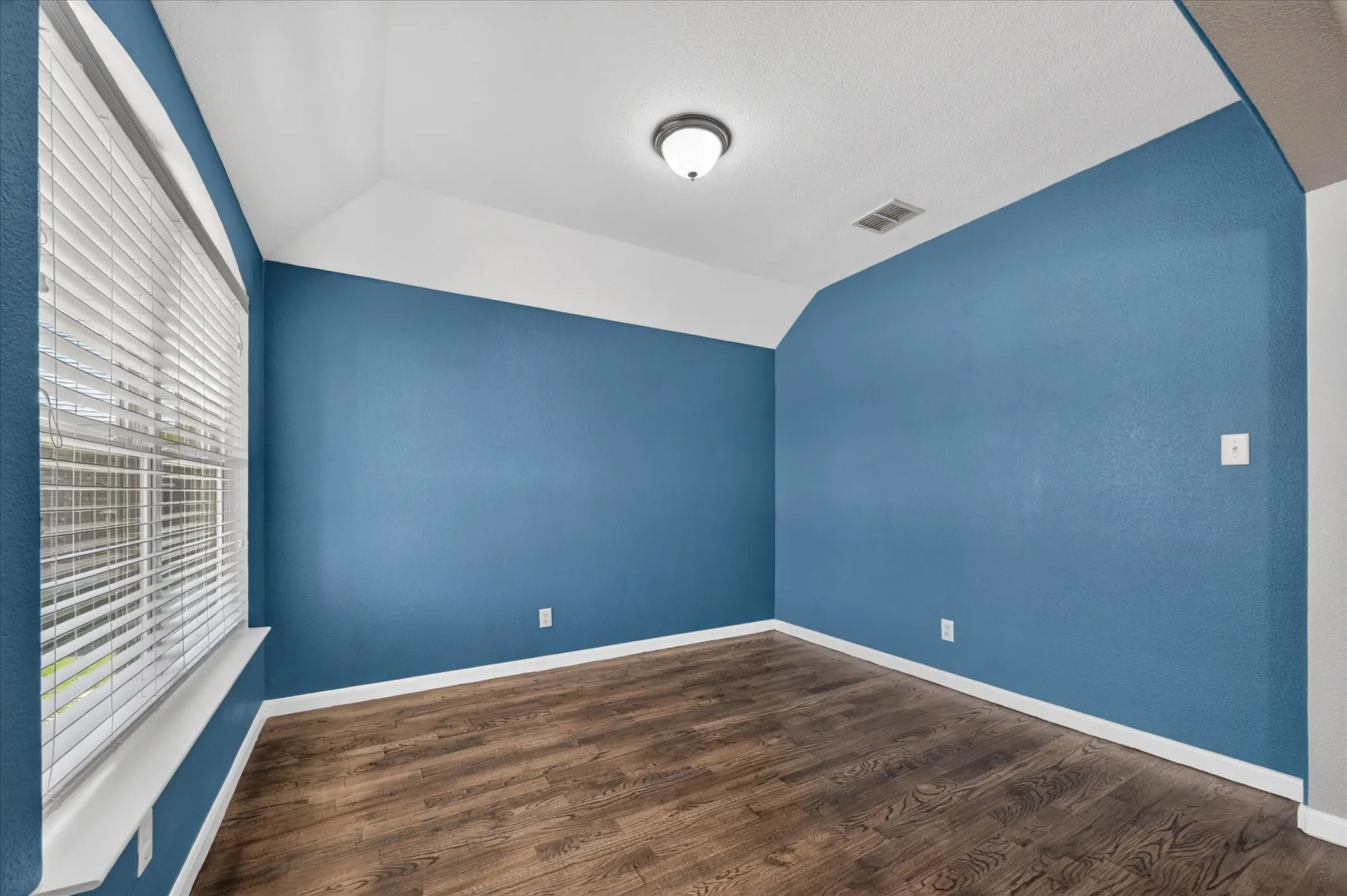 Vaulted ceiling, wood-finish flooring, and a window with horizontal blinds