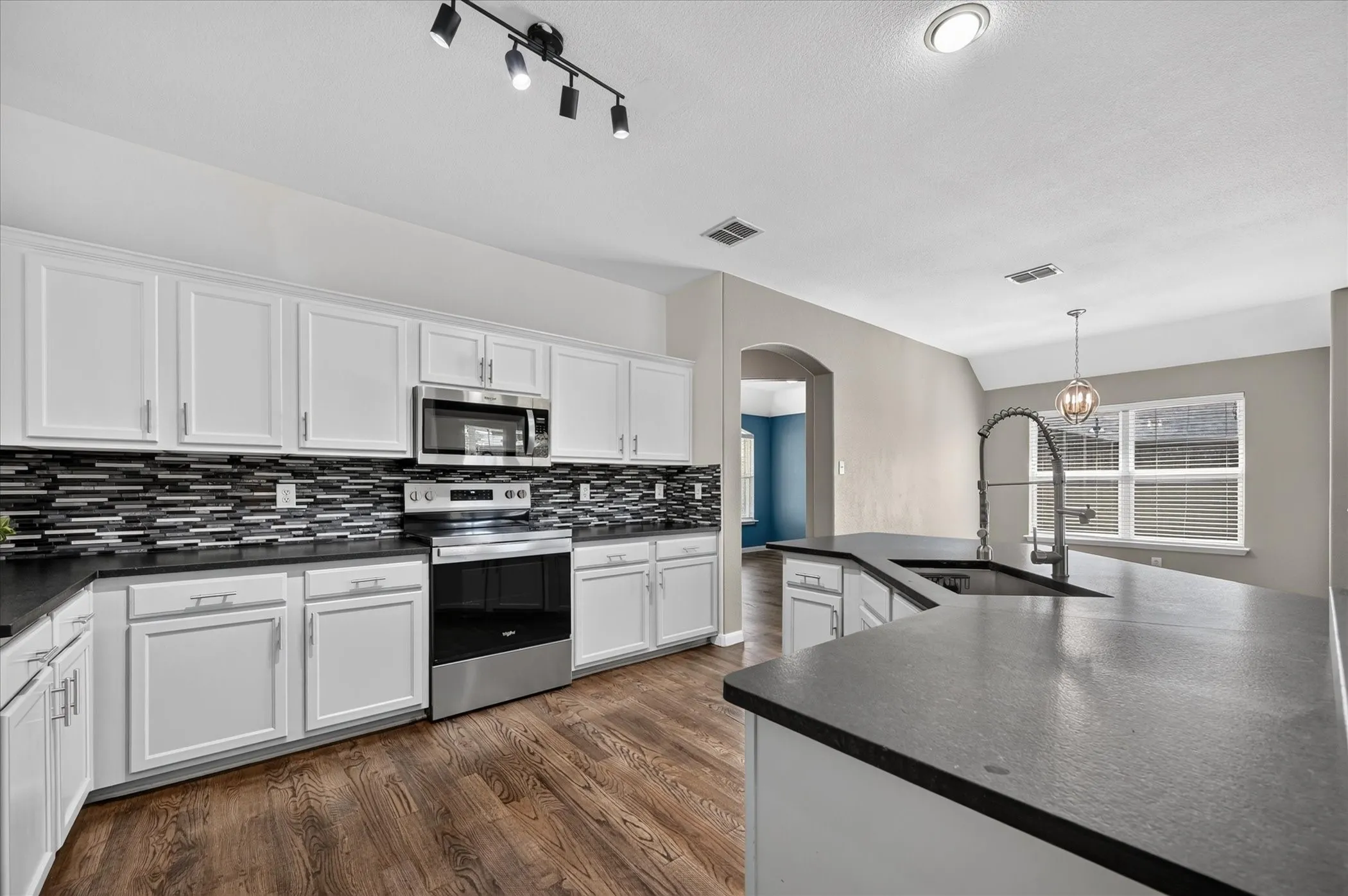 Kitchen featuring white cabinetry, dark countertops, a mosaic tile backsplash, stainless steel appliances, and wood-finish flooring