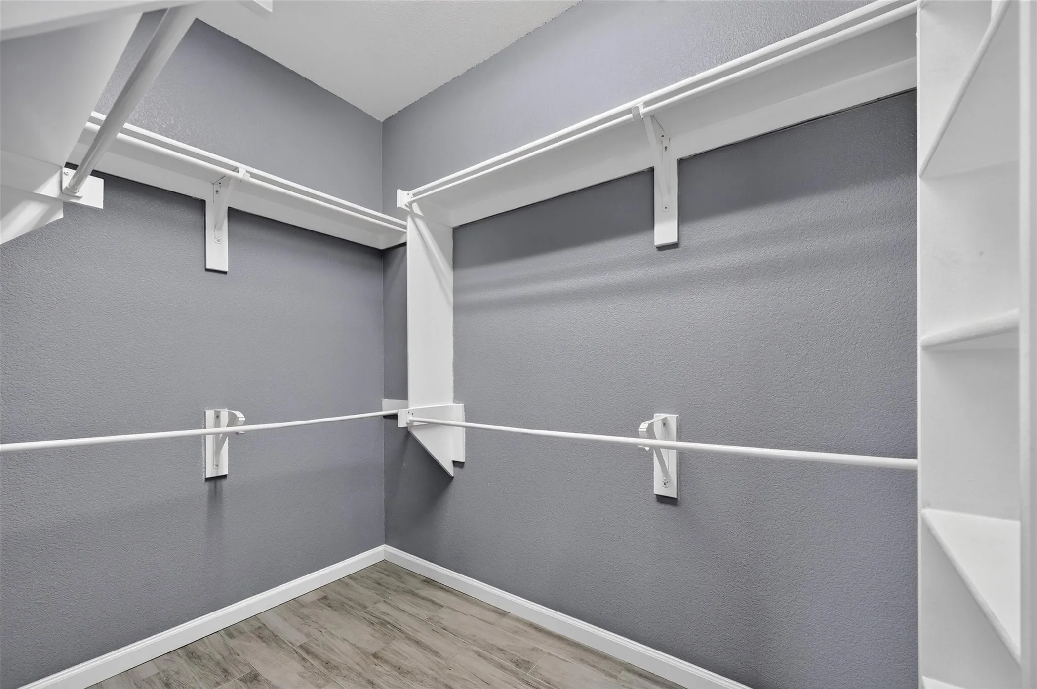 Spacious walk-in closet featuring dual track lighting systems, white metal rod infrastructure, multiple hanging levels, and wood-finish flooring throughout
