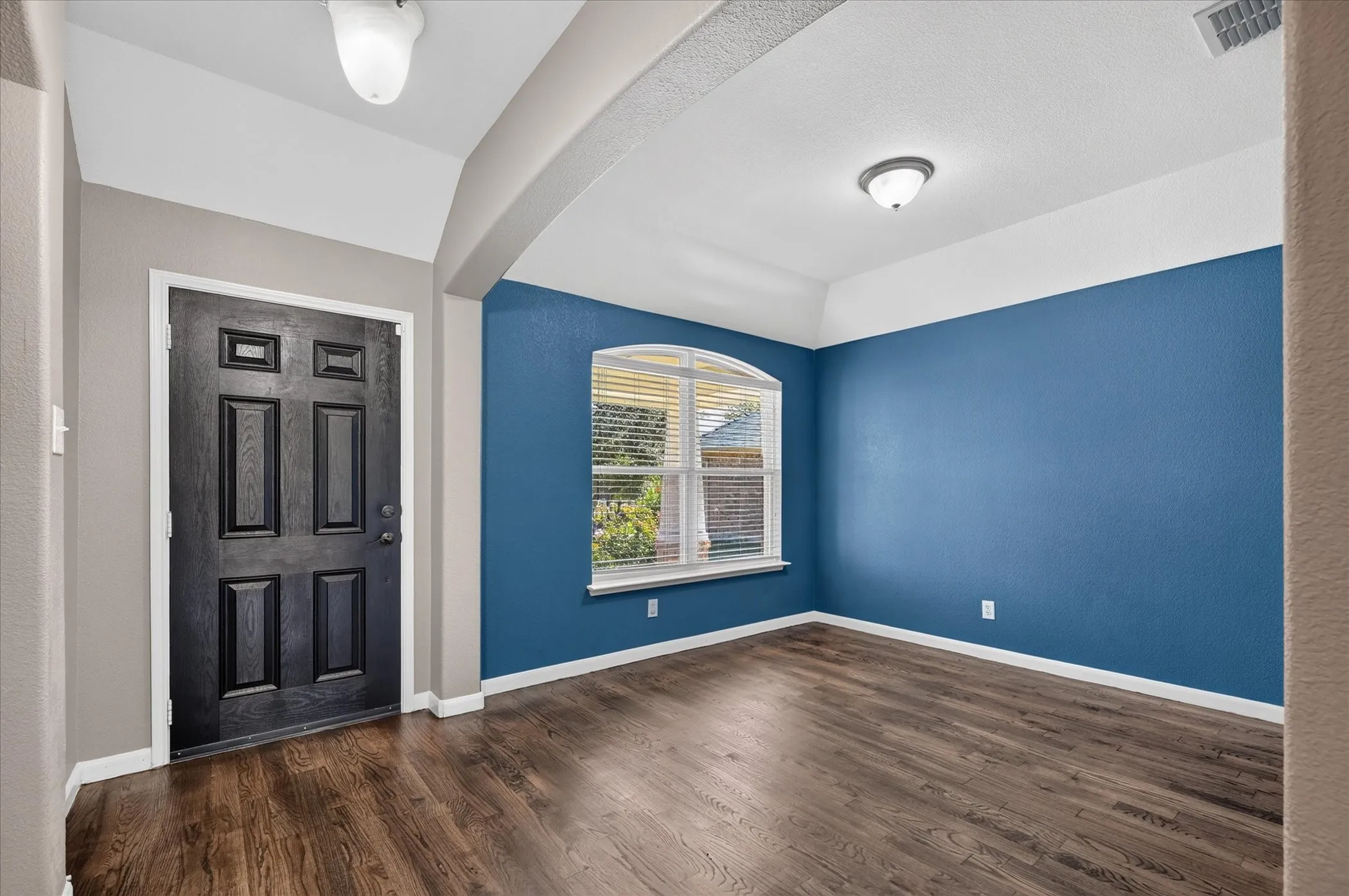 Wood-finish flooring throughout, with a paneled entry door and an arched window