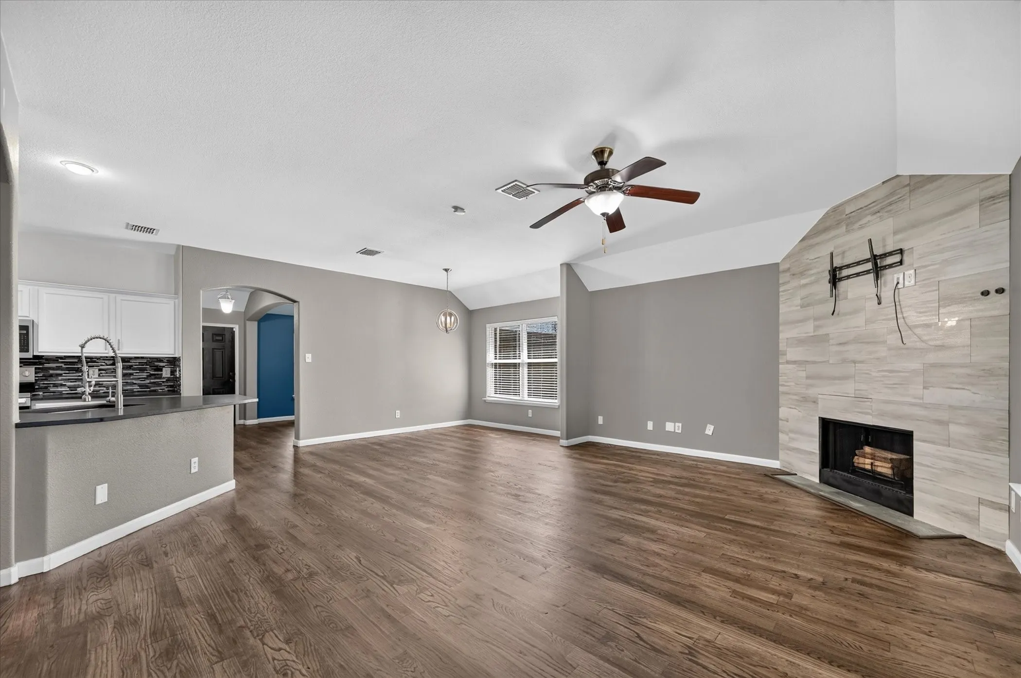 Spacious living area featuring wood-finish flooring, a tiled fireplace, and a ceiling fan