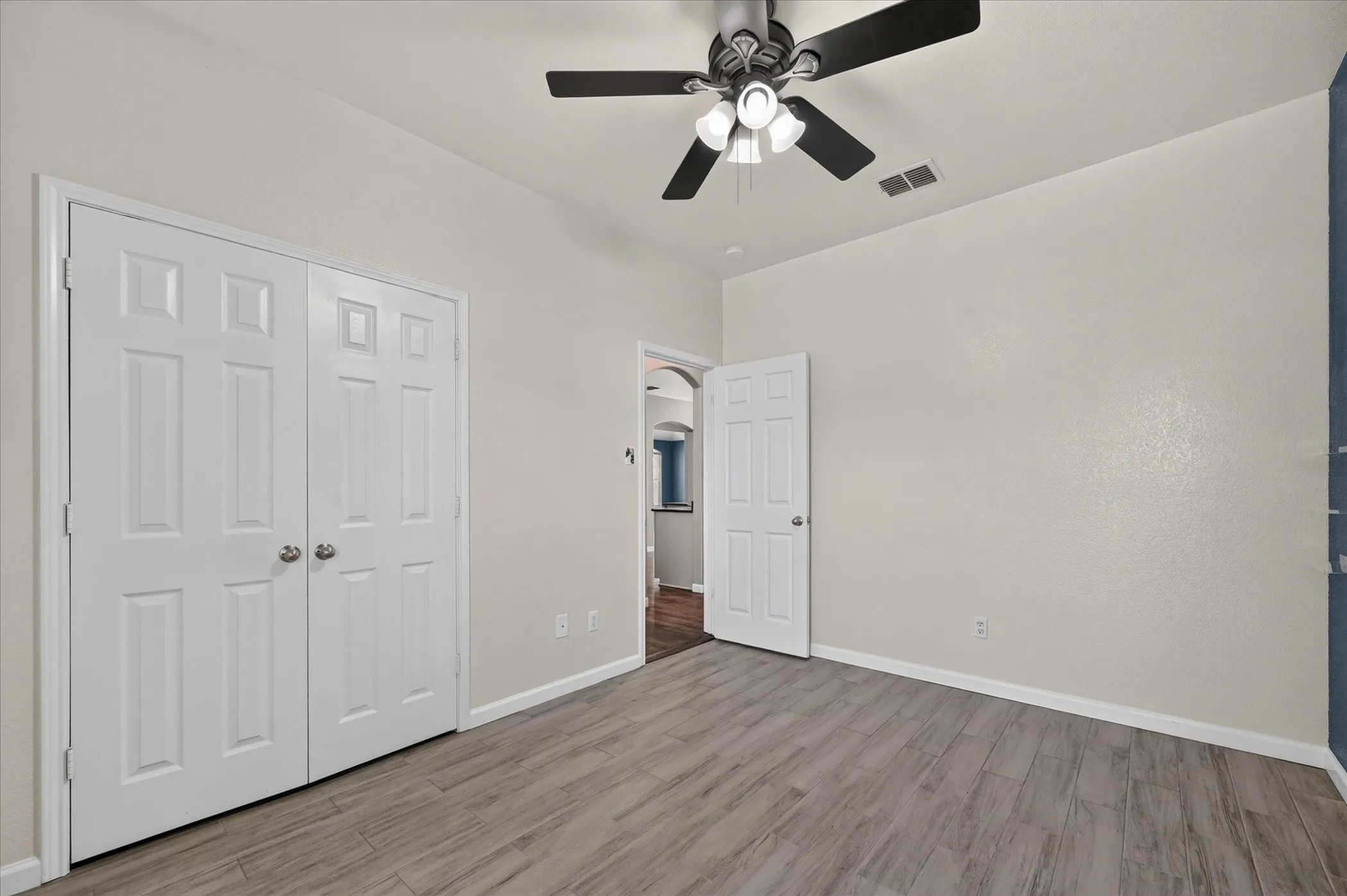 Wood-finish flooring, ceiling fan with integrated lighting, paneled doors, and neutral wall tones