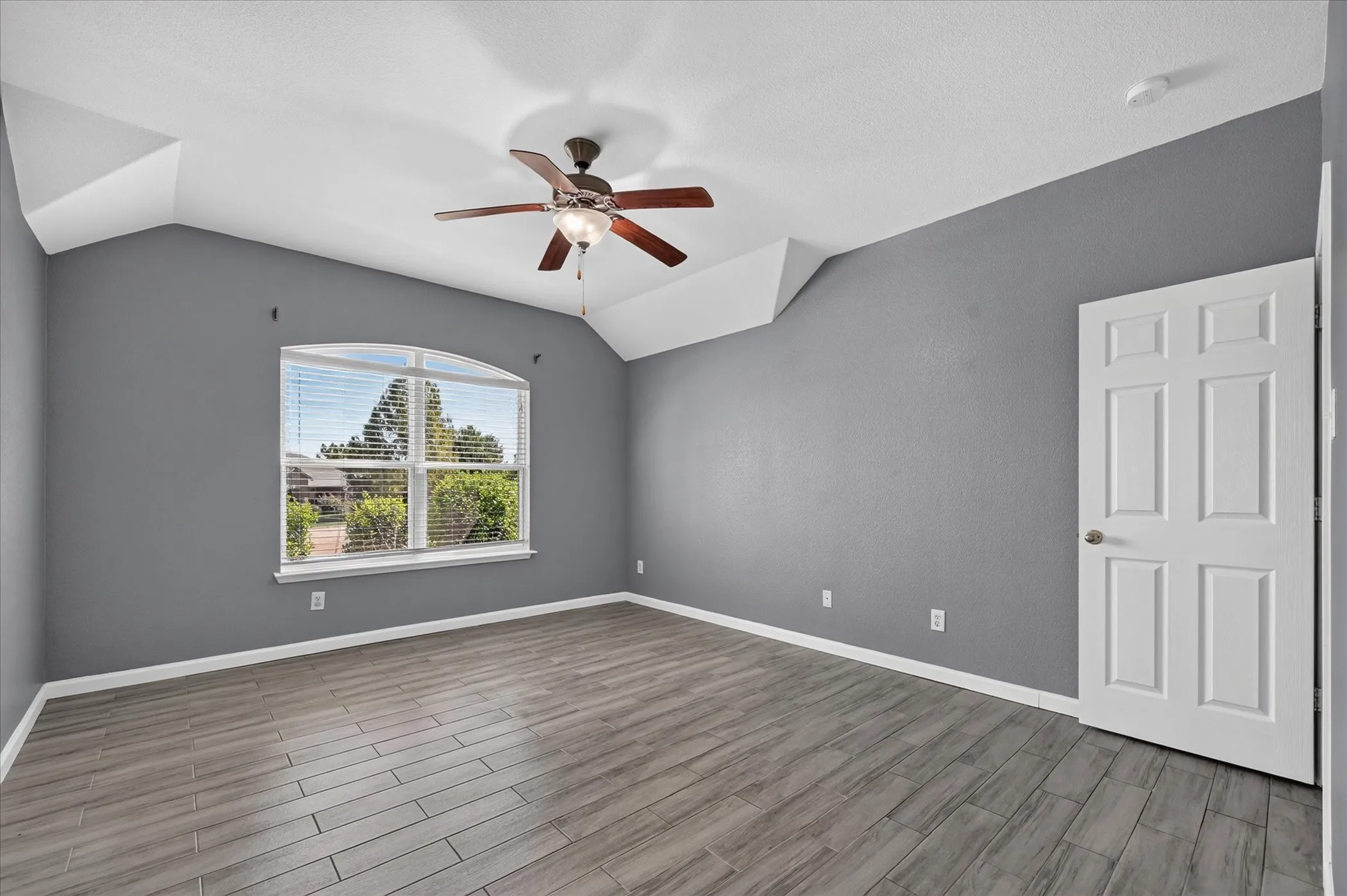 Vaulted ceiling with a ceiling fan, wood-finish flooring, and an arched window