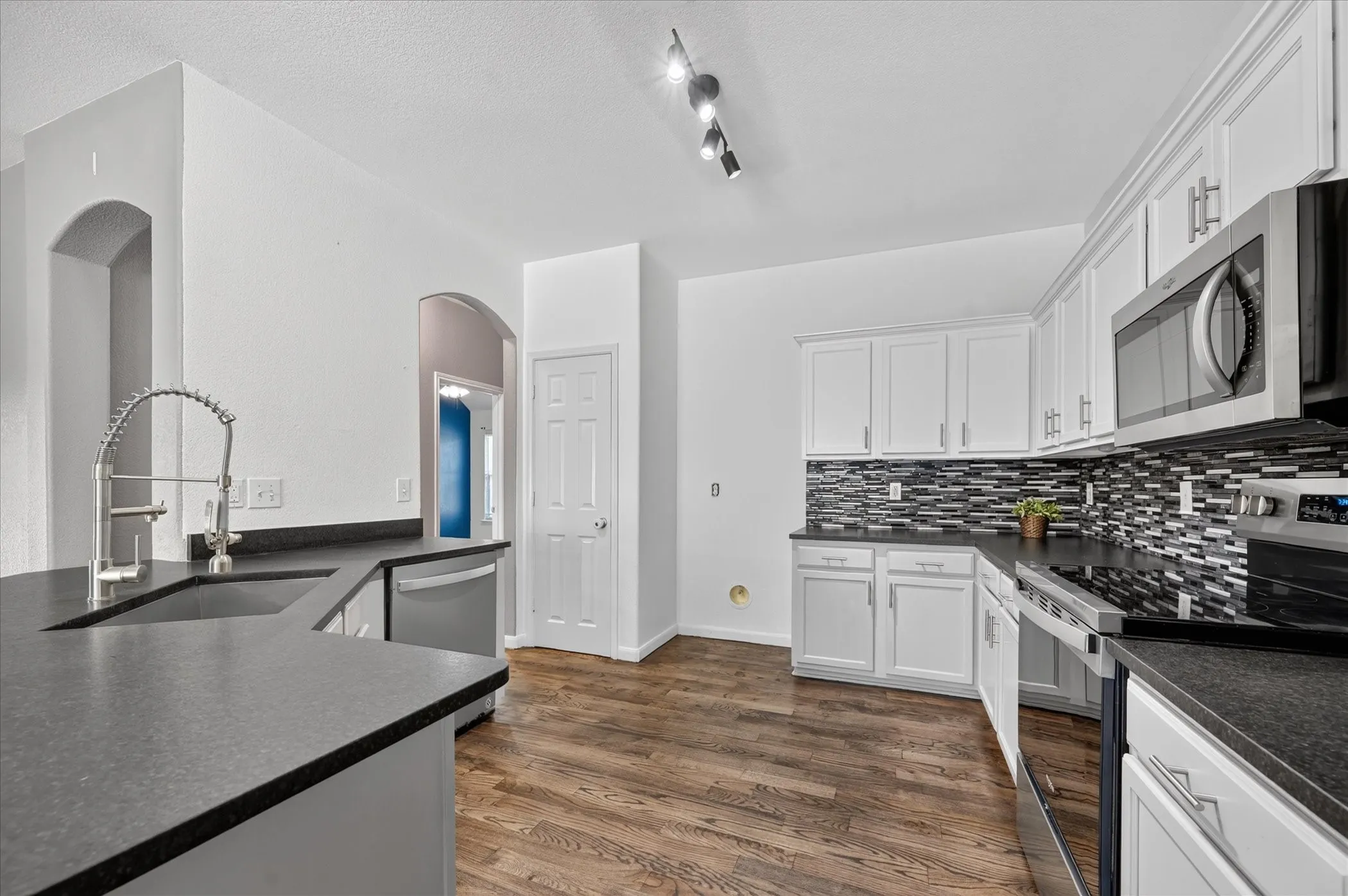 Kitchen featuring white cabinetry, dark countertops, a mosaic tile backsplash, stainless steel appliances, and wood-finish flooring