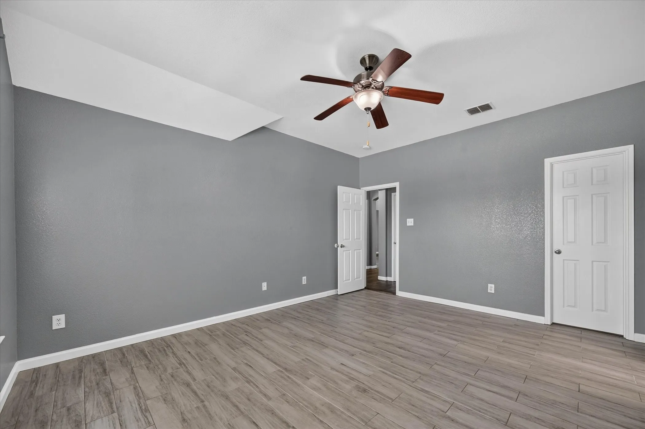 Wood-finish plank flooring, gray painted walls, and a ceiling fan with light fixture