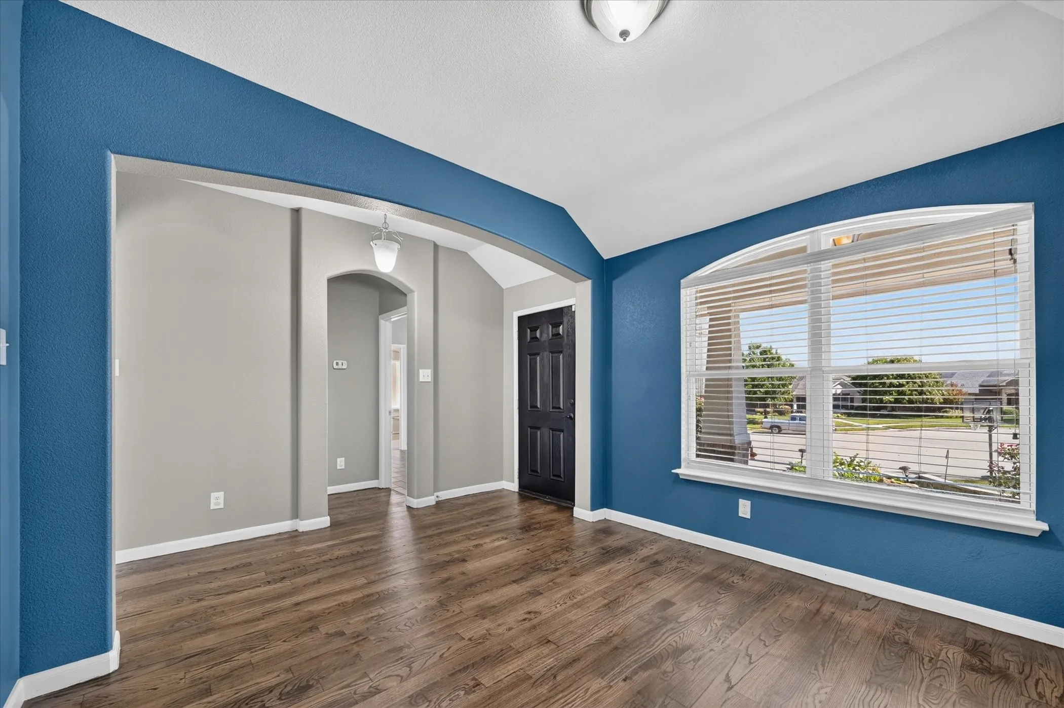 Wood-finish flooring, arched entryway, vaulted ceiling, recessed lighting, and a large arched window with blinds