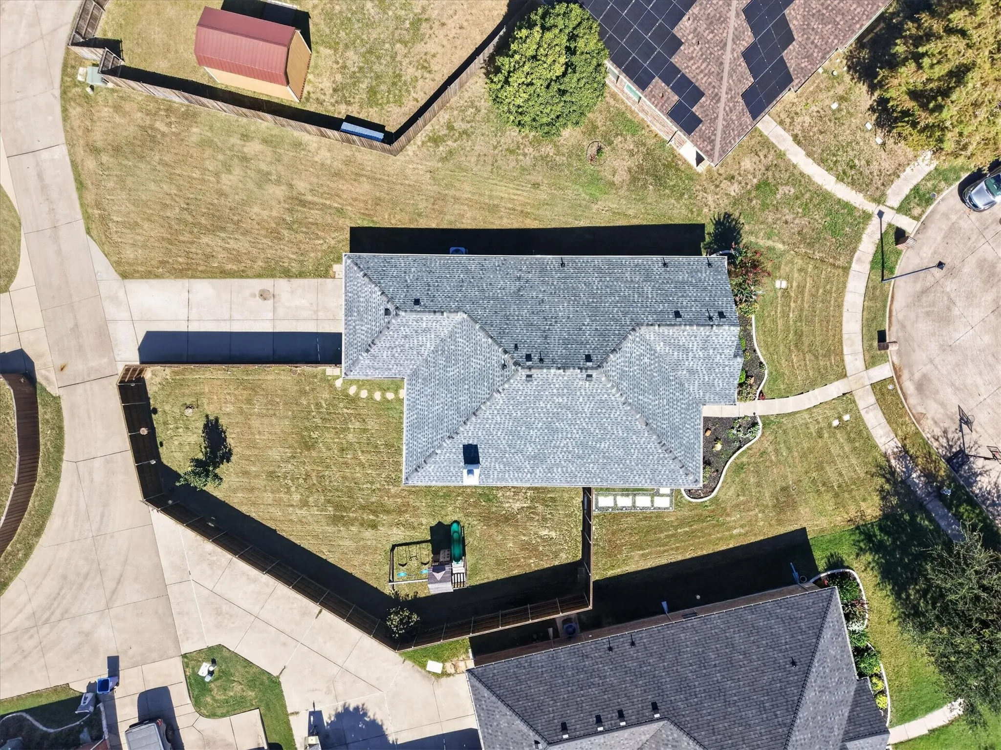 Gable roofline with asphalt shingles, concrete driveway, and a fenced backyard with a storage shed