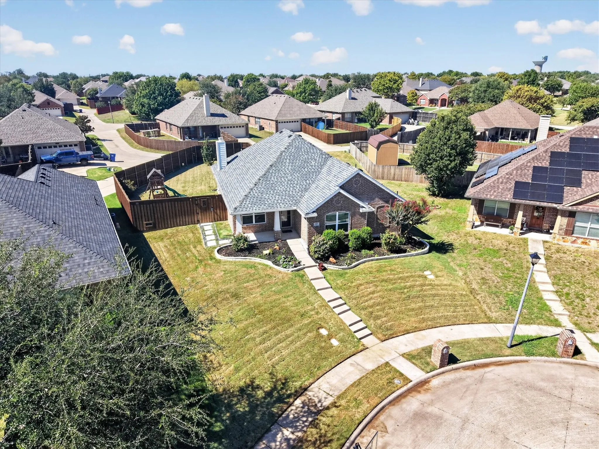 Expansive manicured lawn with mature landscaping and curved hardscape pathways, anchored by a charcoal-toned architectural shingle roof