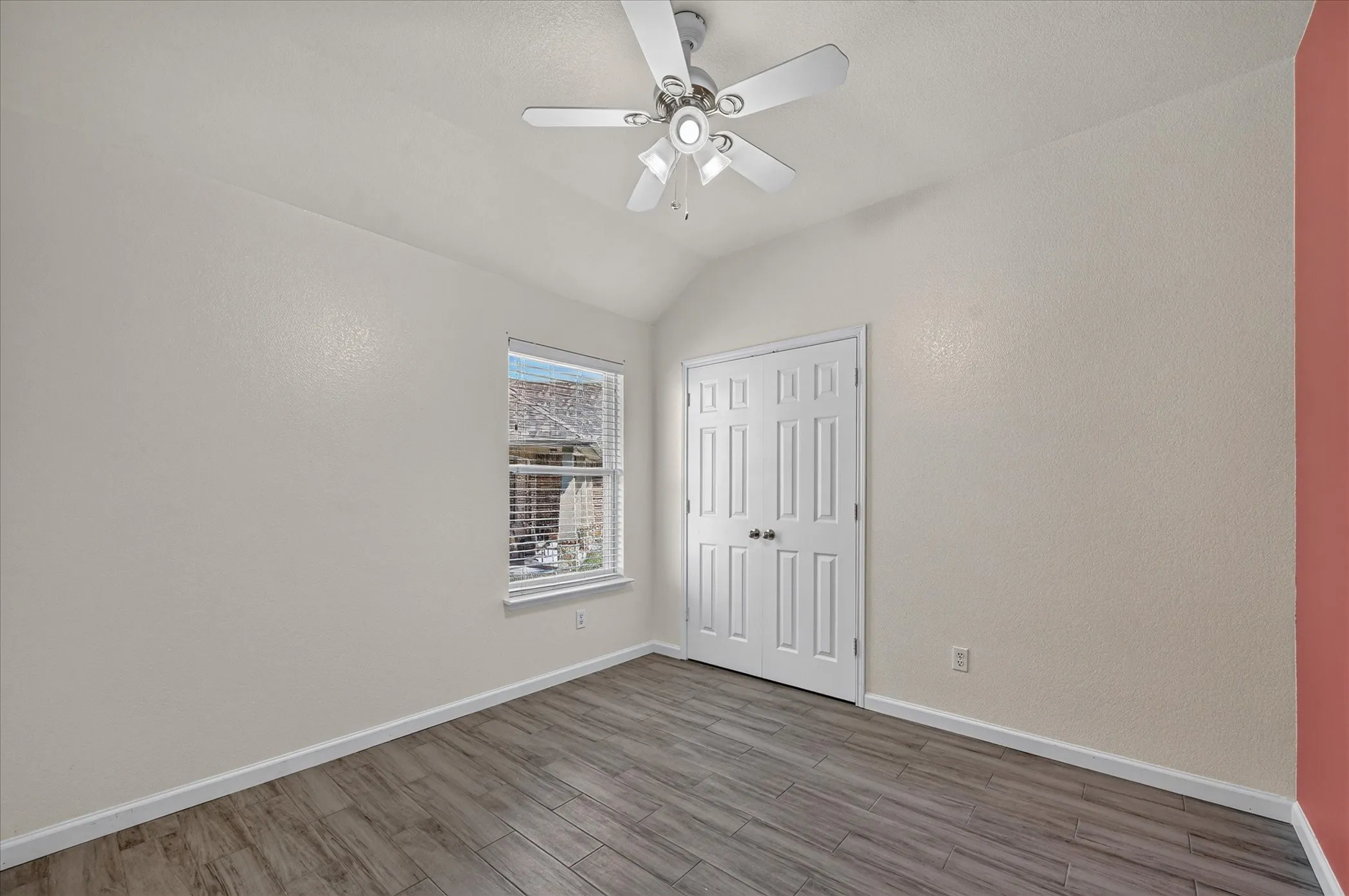 Vaulted ceiling with a ceiling fan, window with blinds, wood-finish flooring, and panel doors