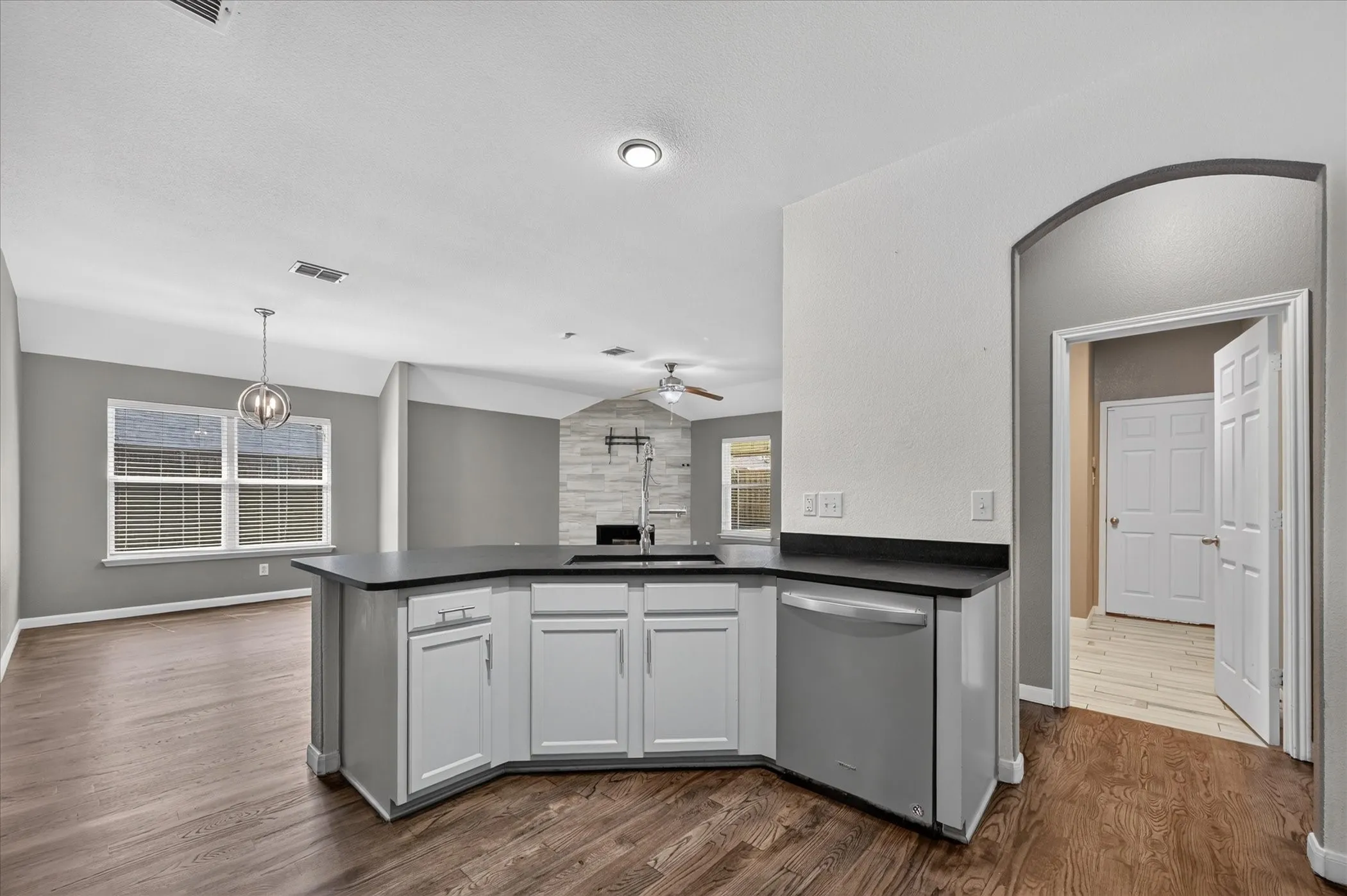 Kitchen island with a dark countertop and white cabinetry, integrated stainless steel dishwasher, wood-finish flooring, and recessed lighting