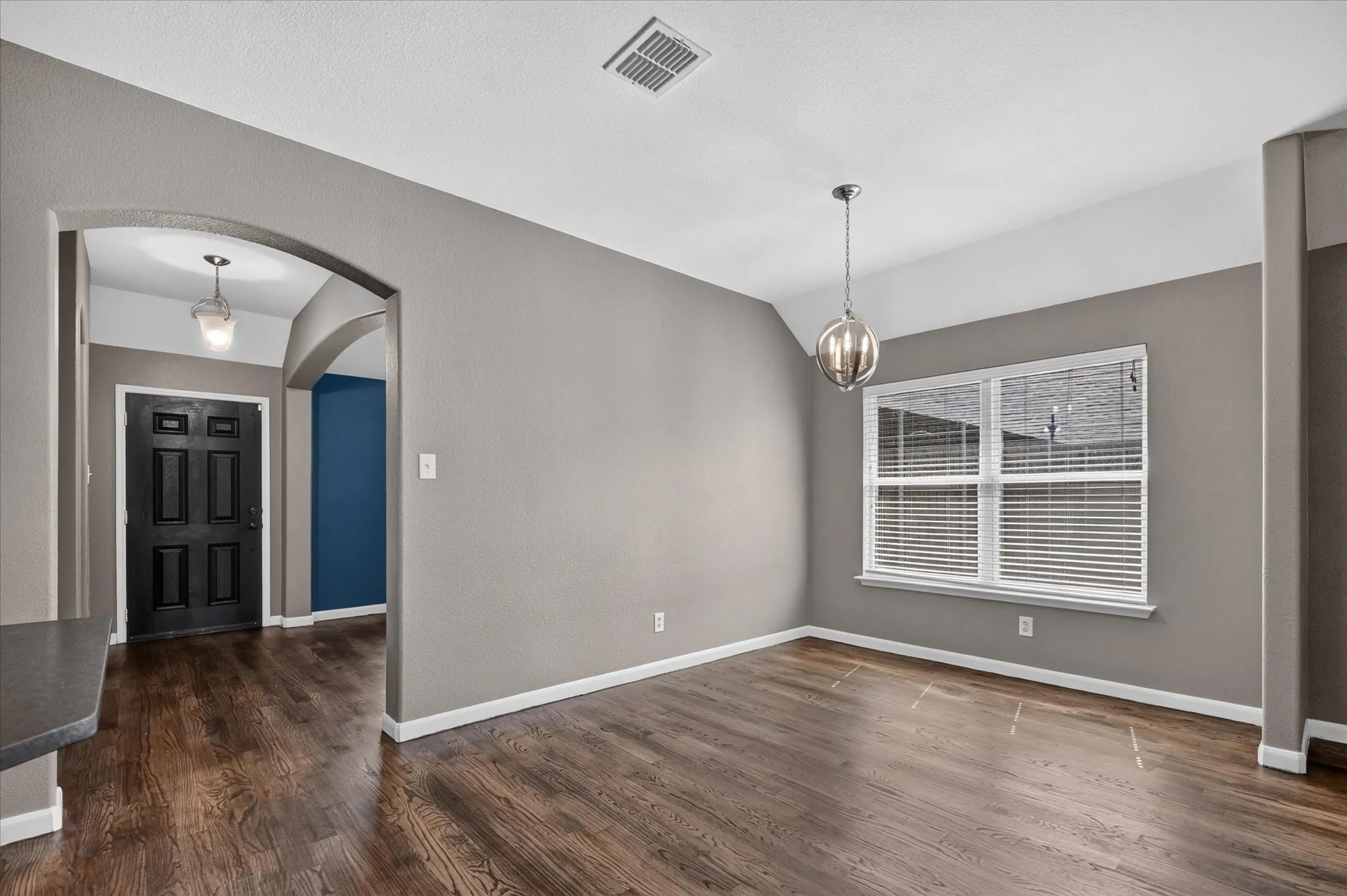 Wood-finish flooring throughout, arched entryway, and a prominent window with blinds