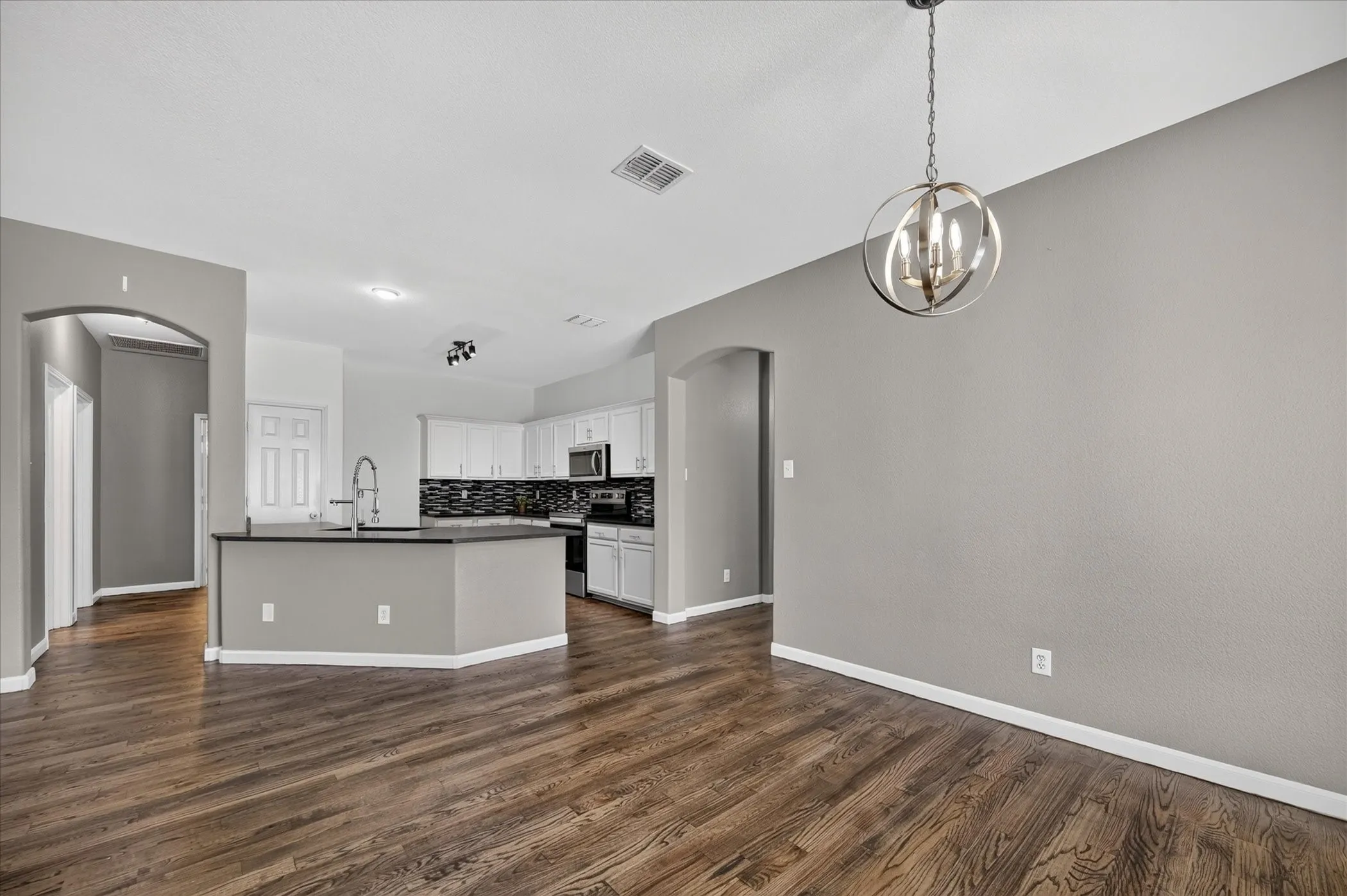 Open-concept living area with dark wood-finish flooring, a contemporary spherical chandelier, and arched doorways