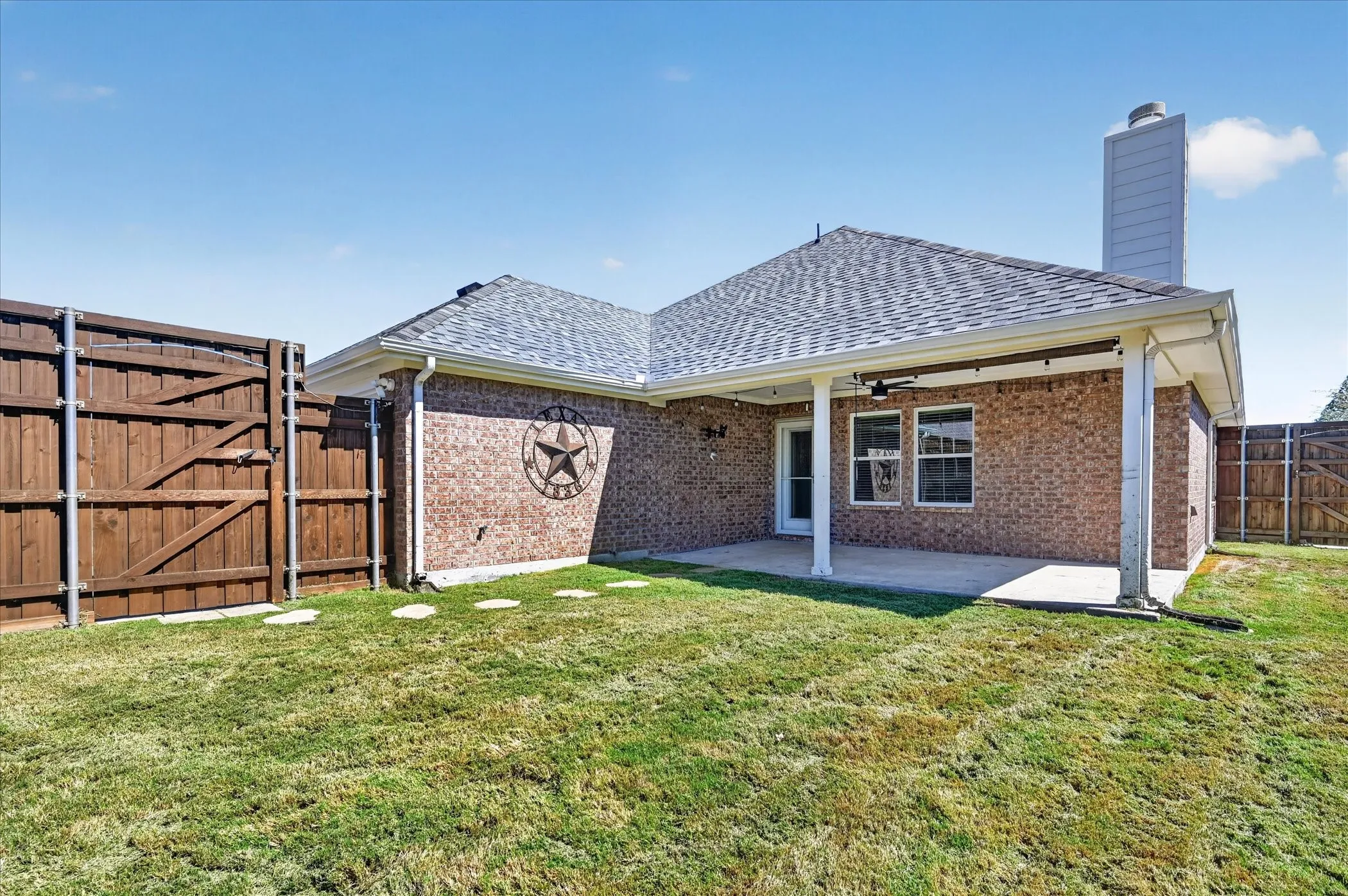 Brick exterior with a covered patio, shingle roof, and a privacy fence