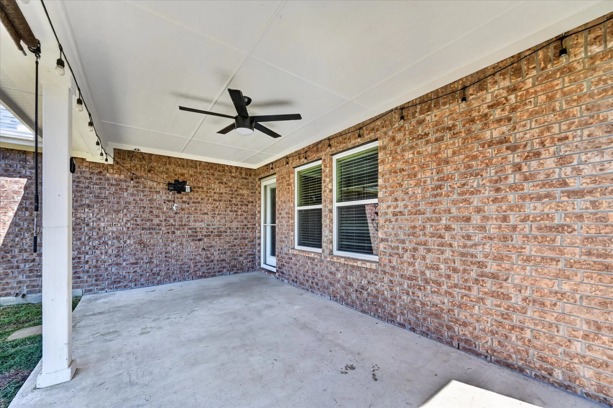 Covered patio with a concrete surface, brick exterior, ceiling fan, and string lighting