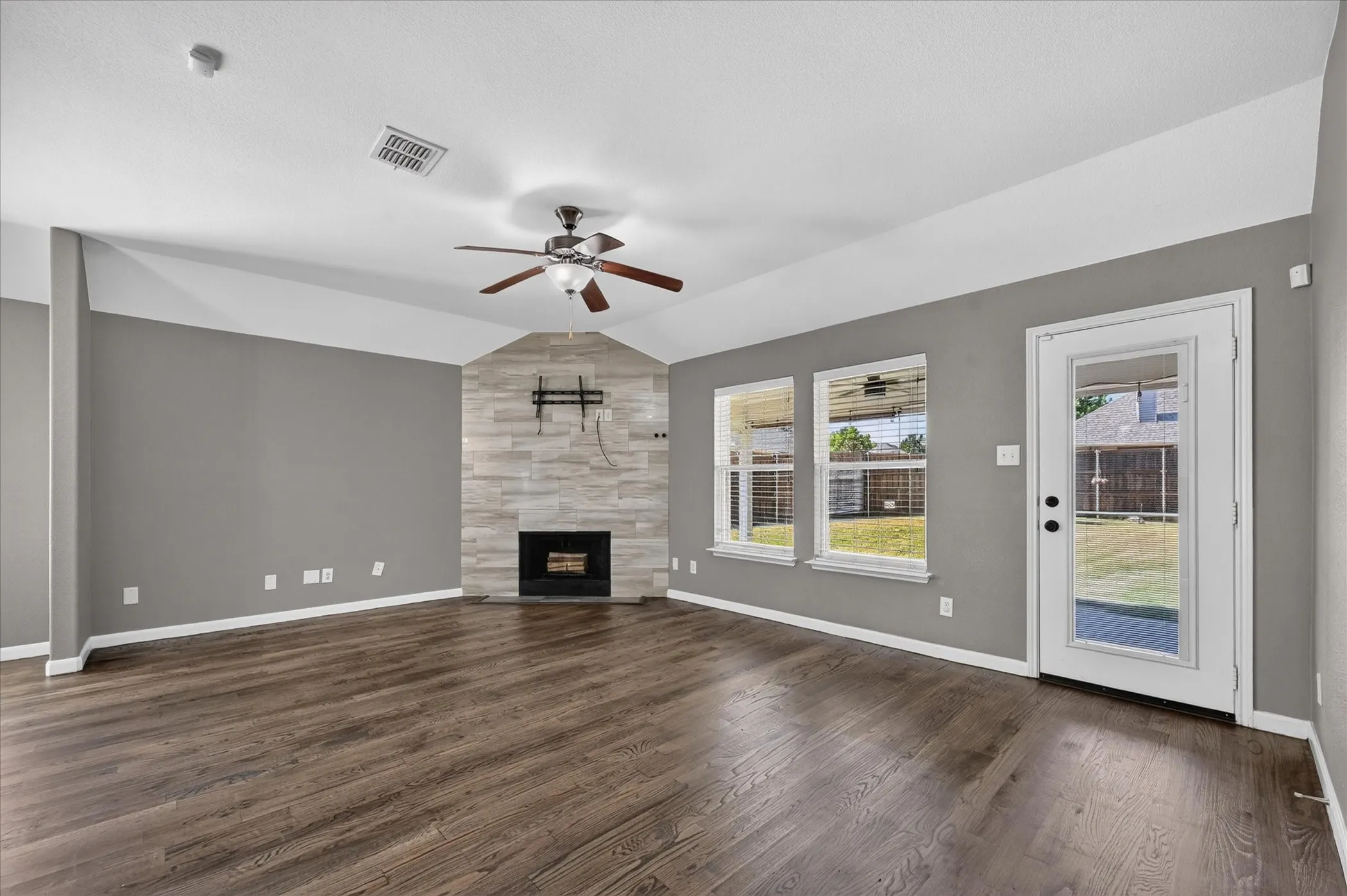 Wood-finish flooring throughout, a vaulted ceiling with a ceiling fan, and a tiled fireplace