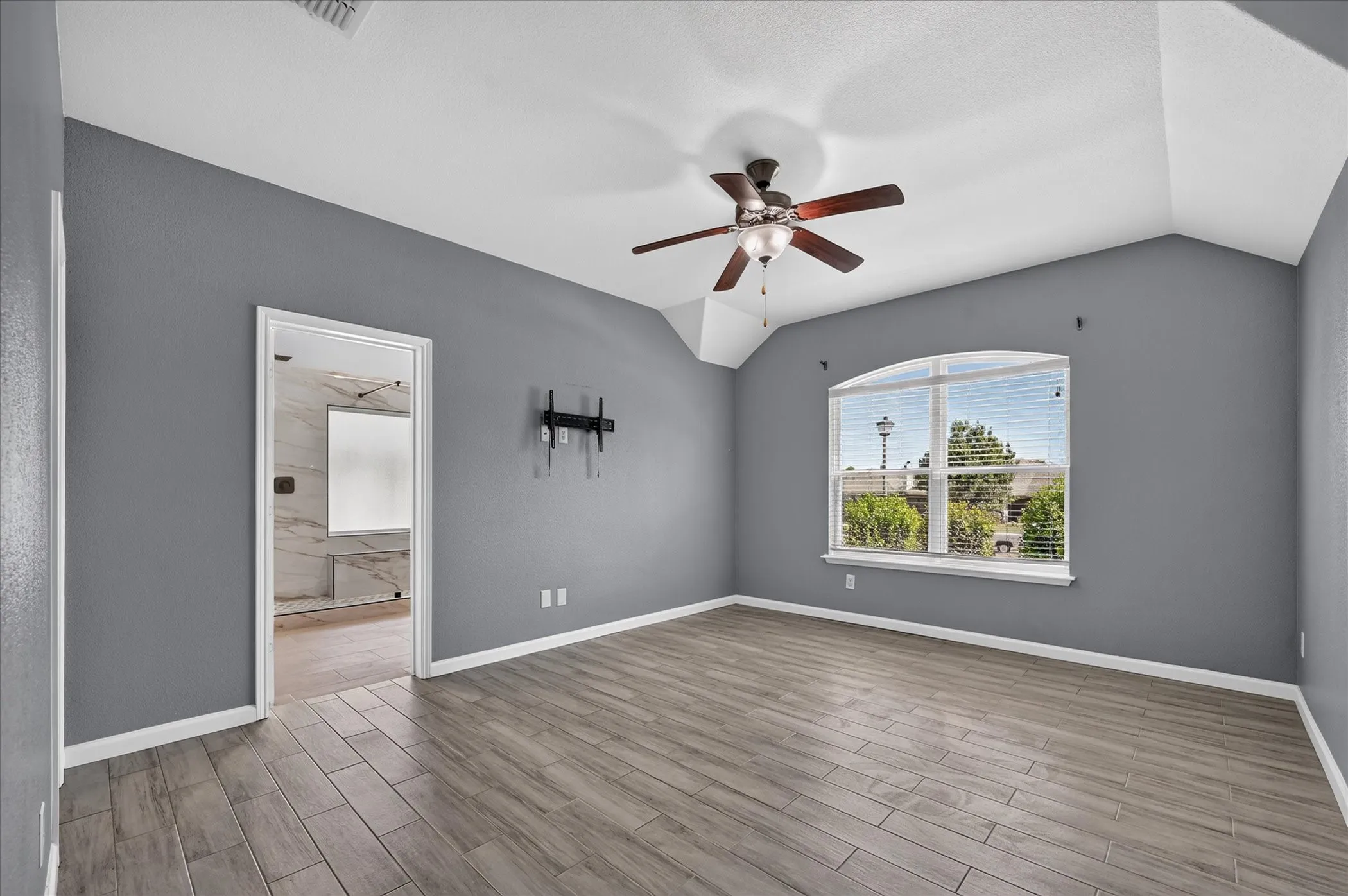 Spacious bedroom with gray walls, wood-finish flooring, and abundant natural light from dual windows