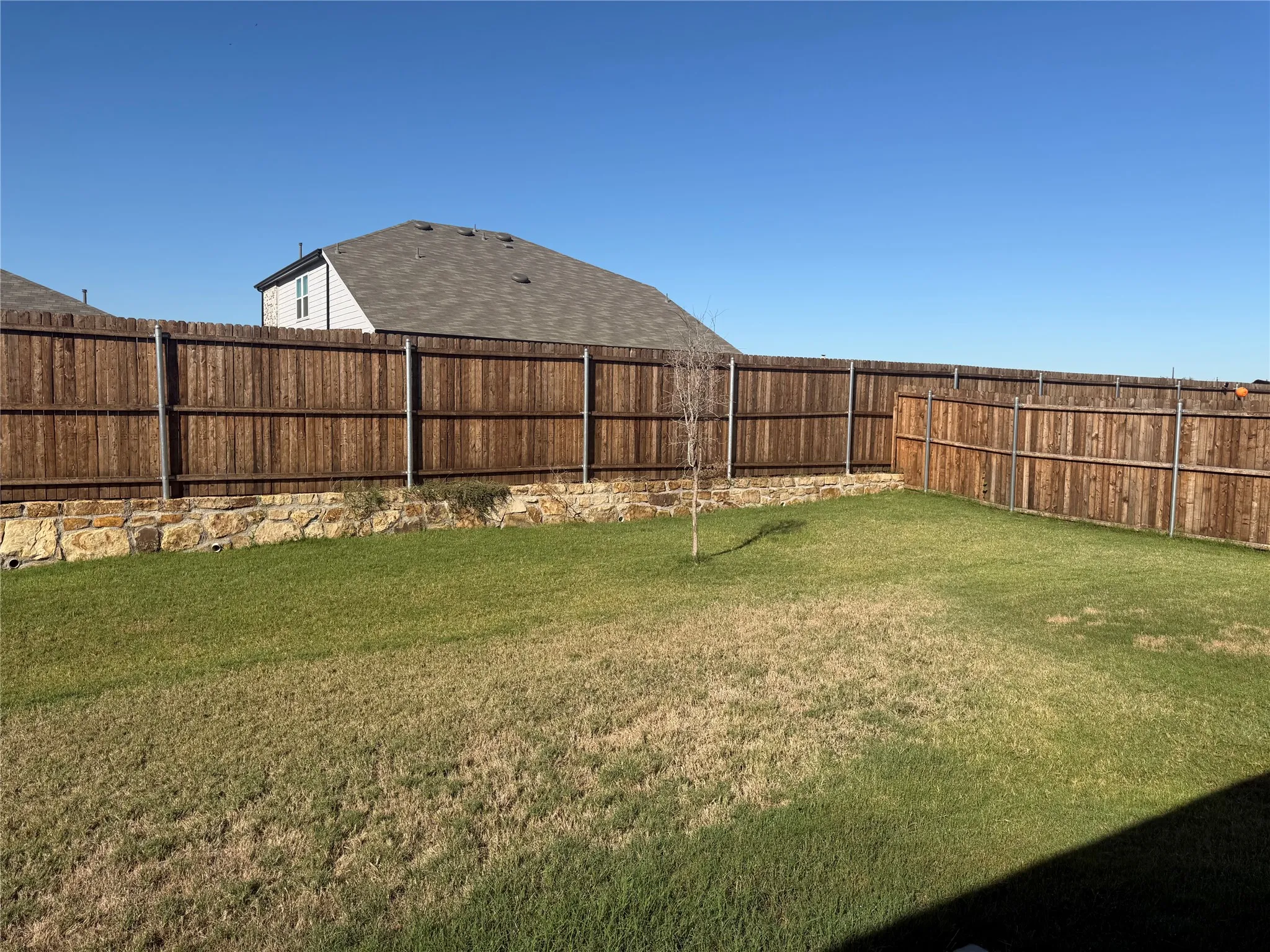 Expansive backyard featuring a wood fence, stone retaining wall, and green lawn
