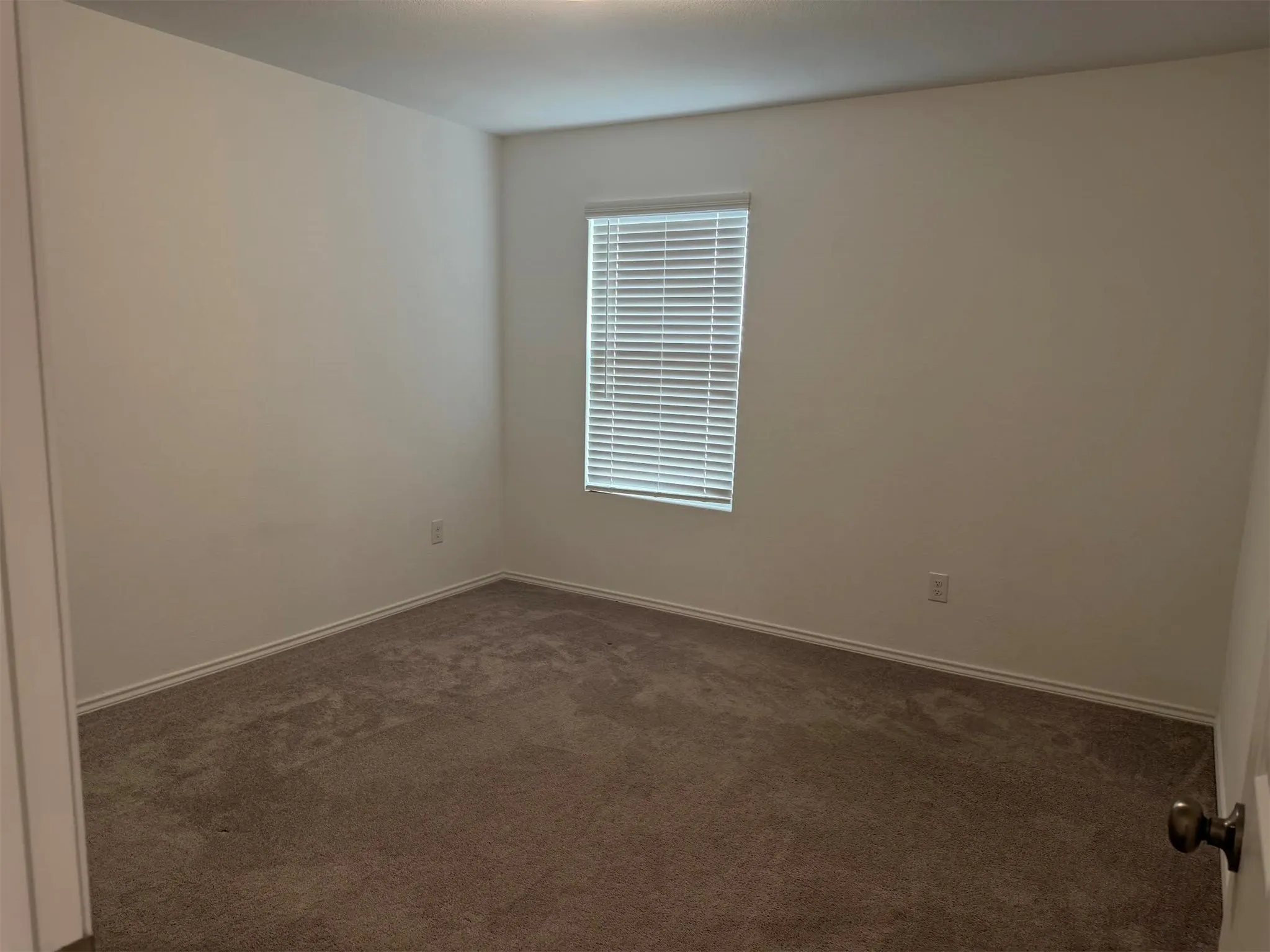 Neutral wall paint, brown carpeting, and a window with horizontal blinds