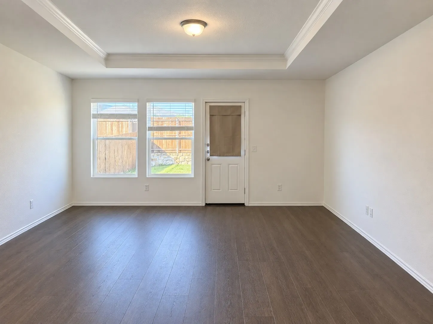 Recessed ceiling with crown molding, wood-finish flooring, multiple windows, and a glass-paneled door