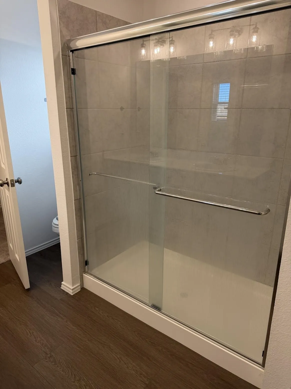 Glass-enclosed shower with gray tiled walls, a white shower base, and a chrome-finish sliding door