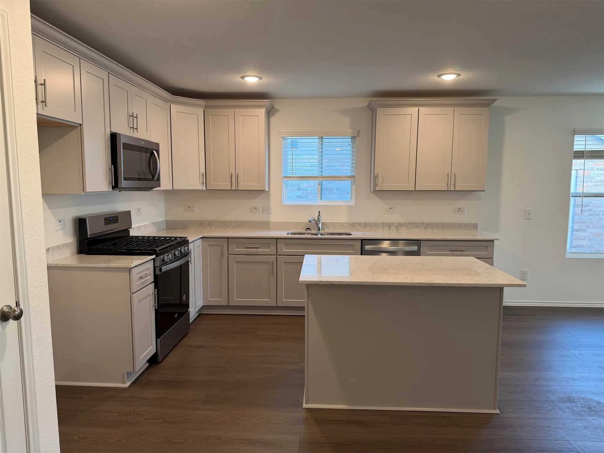 Kitchen featuring wood-finish flooring, light-toned cabinetry, stainless steel appliances, and a central island with a light-toned countertop