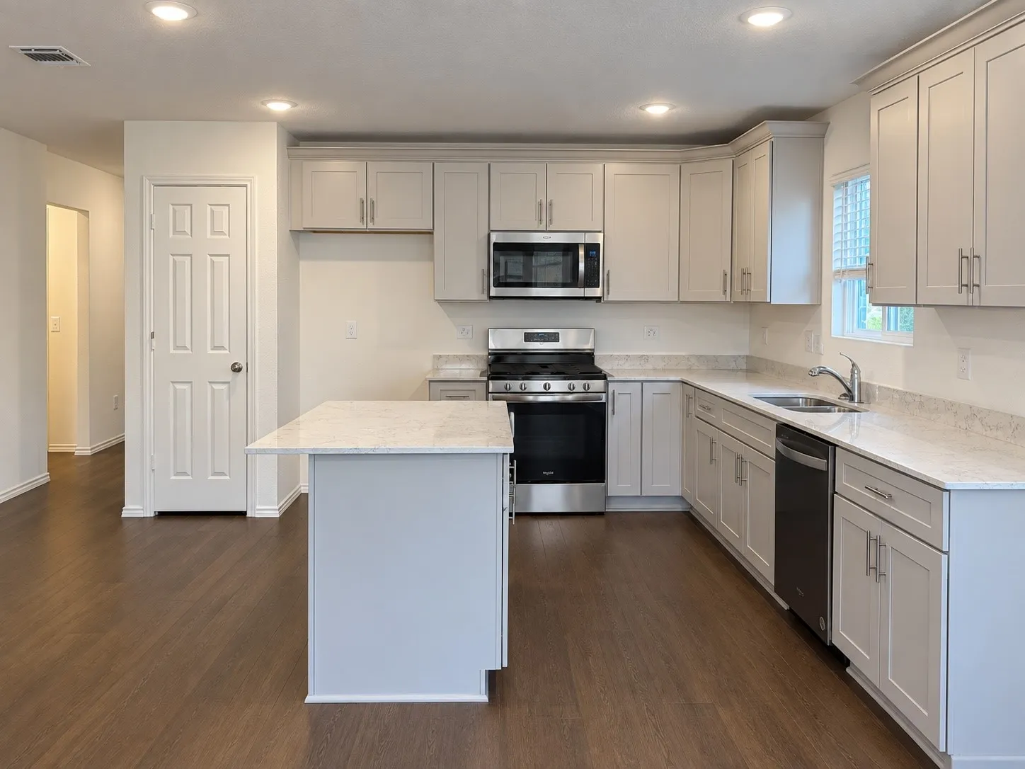 Kitchen featuring wood-finish flooring, recessed lighting, a central island, light-toned cabinetry, and stainless steel appliances