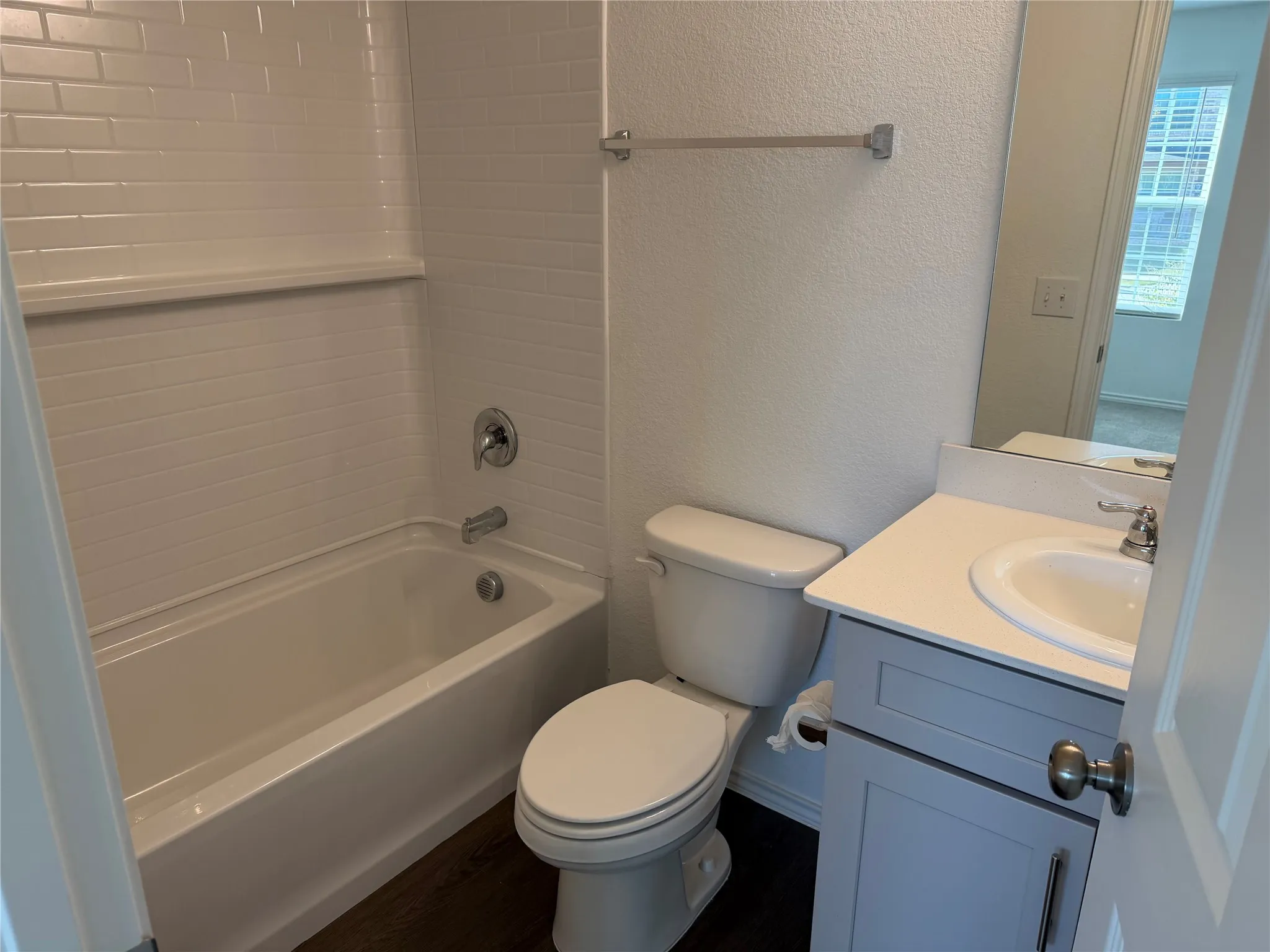 White subway tile shower surround with integrated shelf, chrome bath fixtures, wood-finish flooring, and a vanity with a white countertop and gray cabinetry