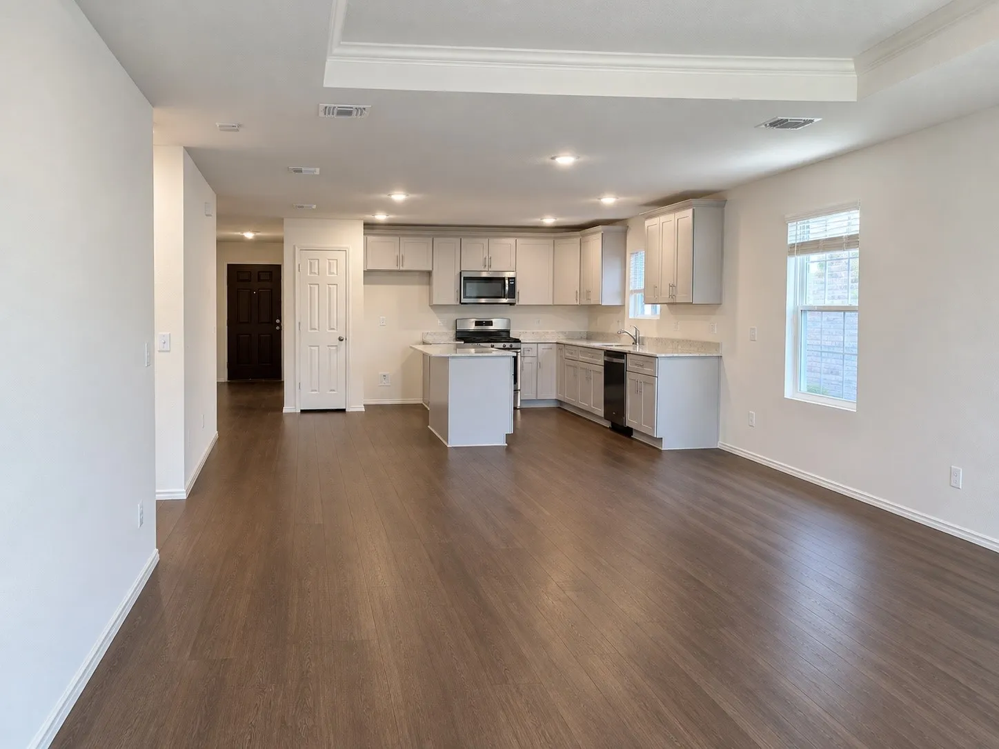 Open-concept living area with wood-finish flooring, recessed lighting, and a tray ceiling