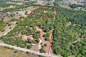 Expansive wooded lot with a detached structure featuring a red roof, bordered by a paved road