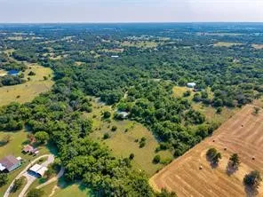 Expansive rural acreage featuring mature tree coverage, open pastureland, and a residential structure with outbuildings situated on the property