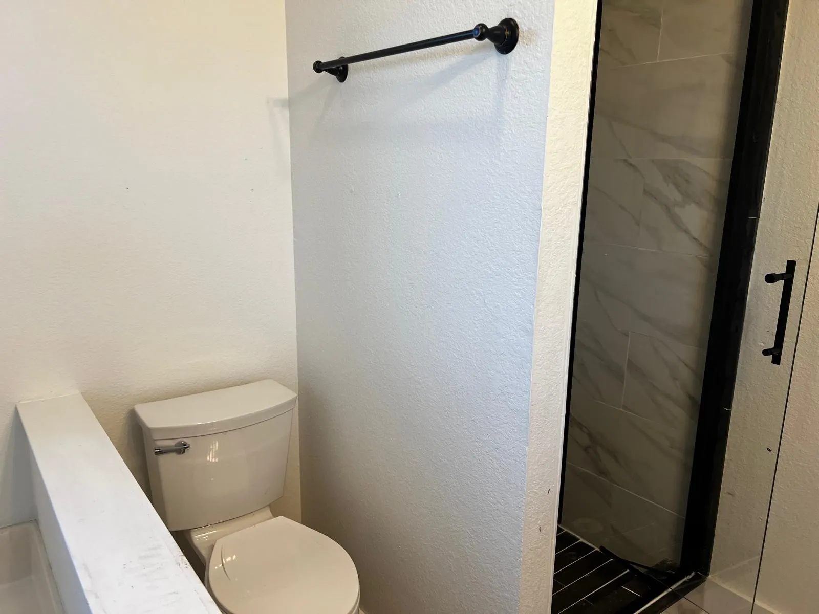 Walk-in shower with clear glass enclosure, matte black framing, and large format wall tiling