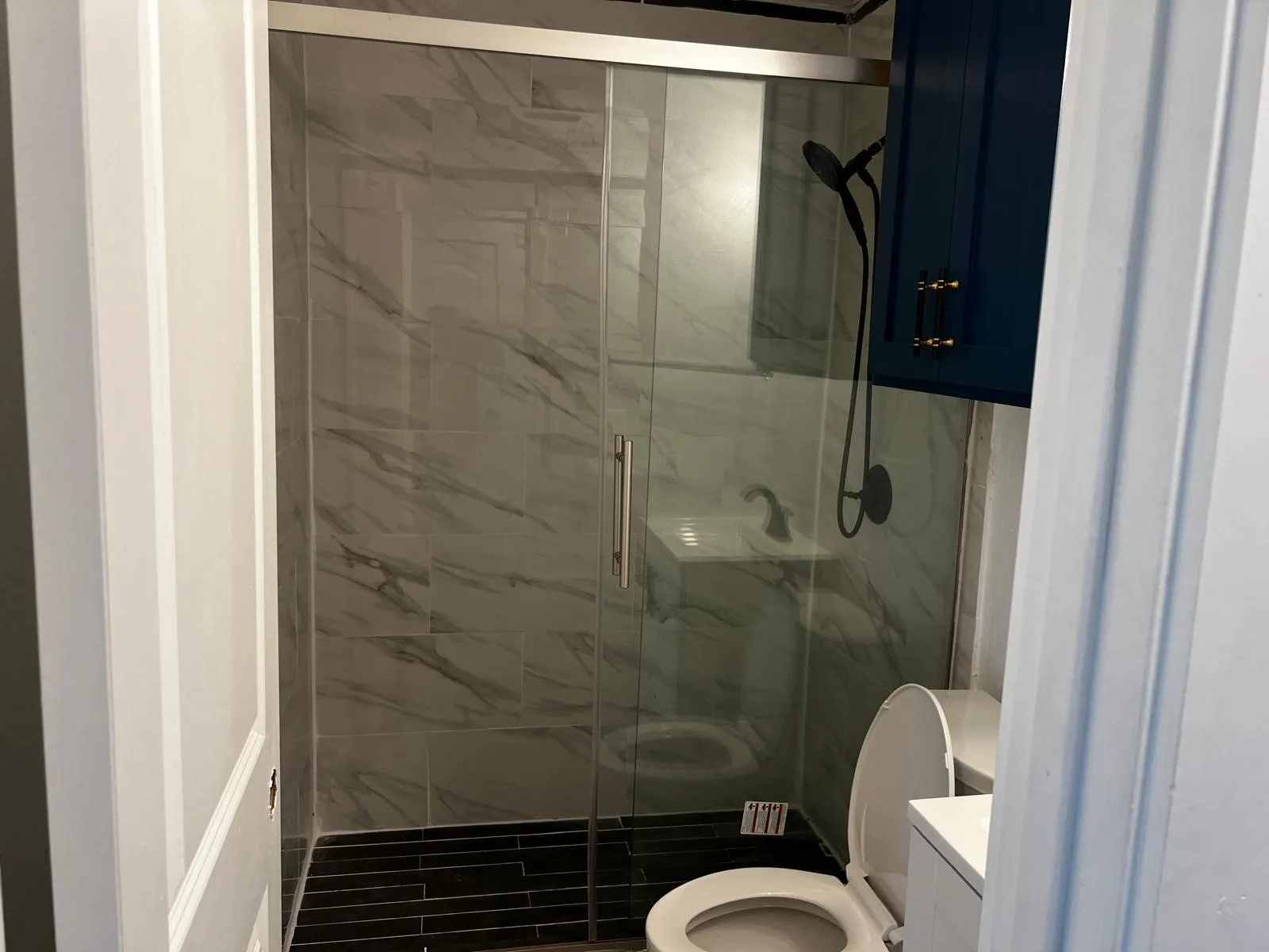 Shower with sliding glass door, marble-patterned wall tile, black tile flooring, and a black shower fixture