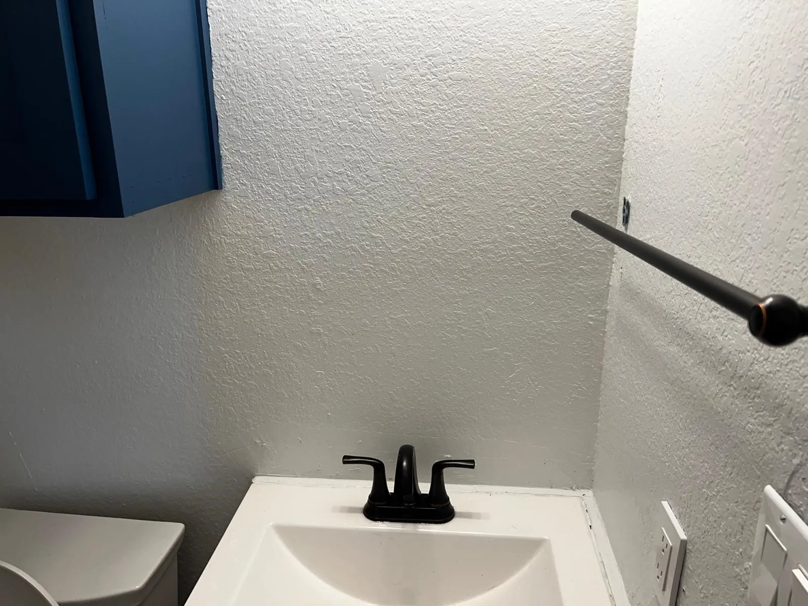 White sink with a matte black faucet, dark blue cabinetry, and a dark metal towel bar