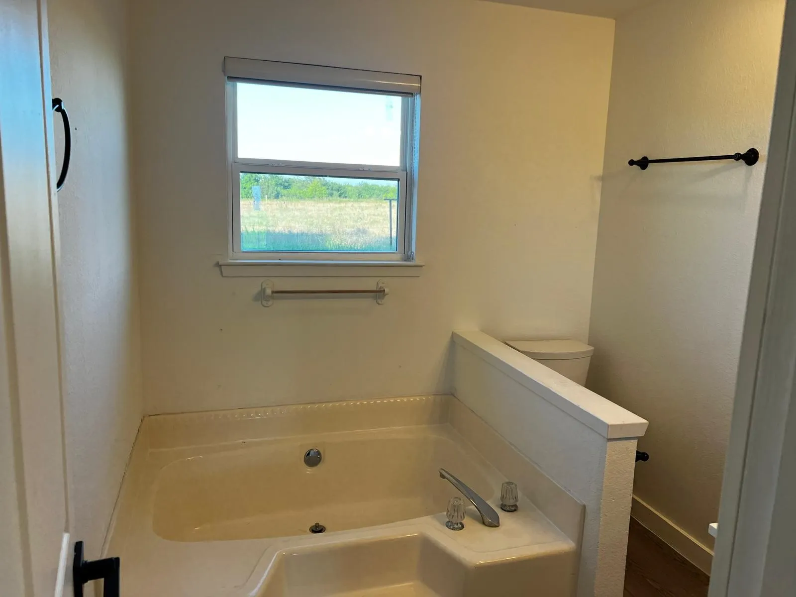 Built-in tub with chrome fixtures, an adjacent window, and a privacy wall