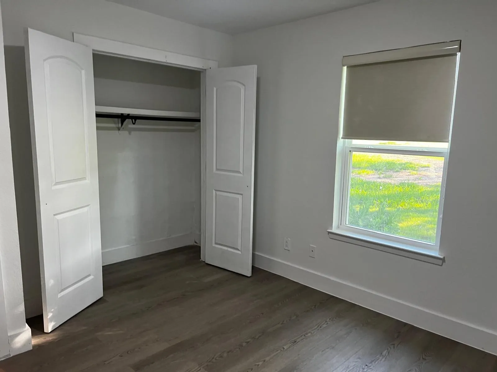 Wood-finish flooring, white walls, and a window with a roller shade