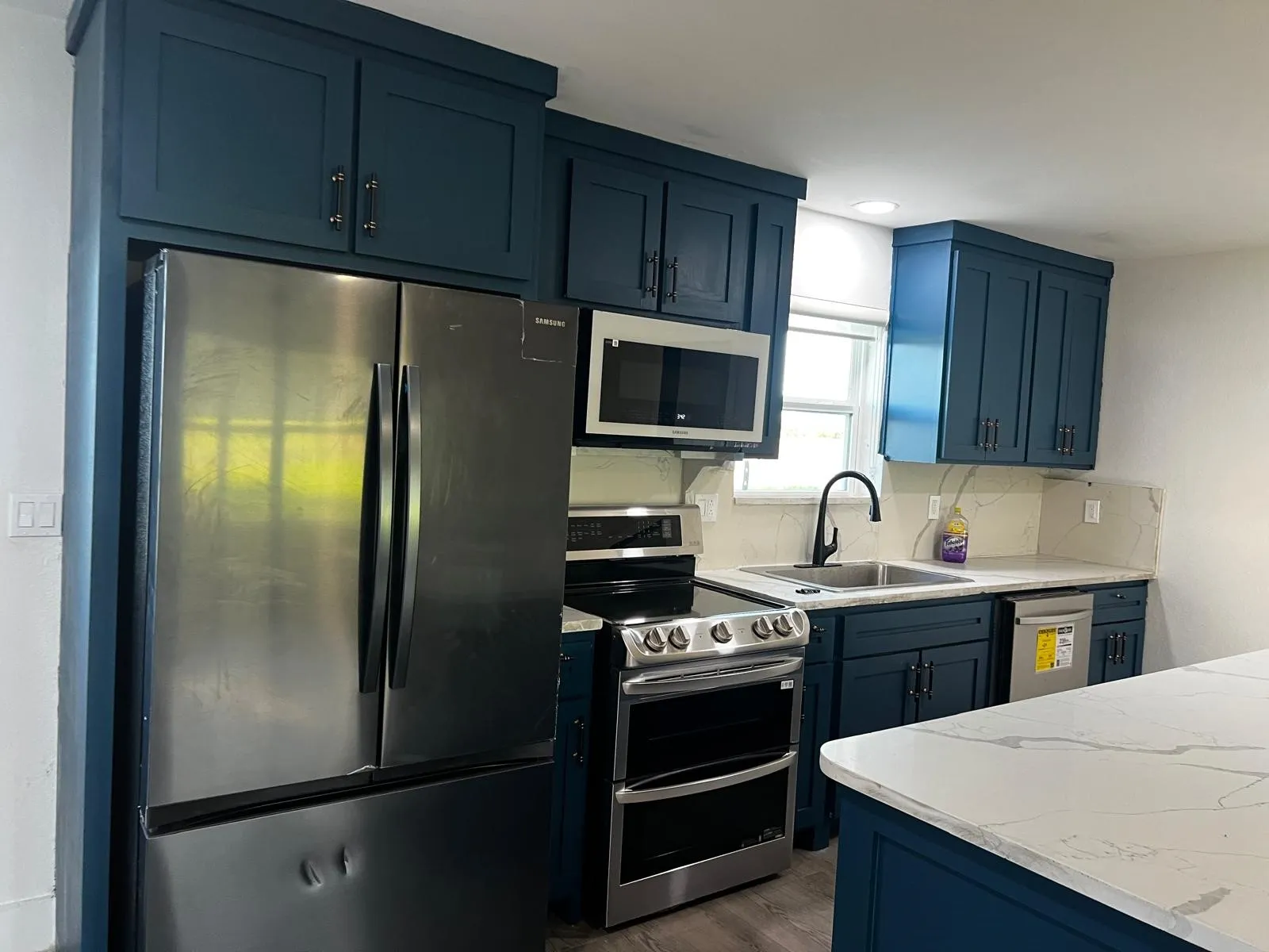 Kitchen featuring deep blue cabinetry, stainless steel appliances, a double oven range, and a white countertop with gray veining