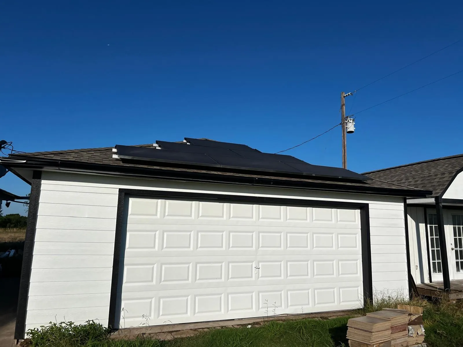 Detached garage with white panel siding, black trim, and solar panels