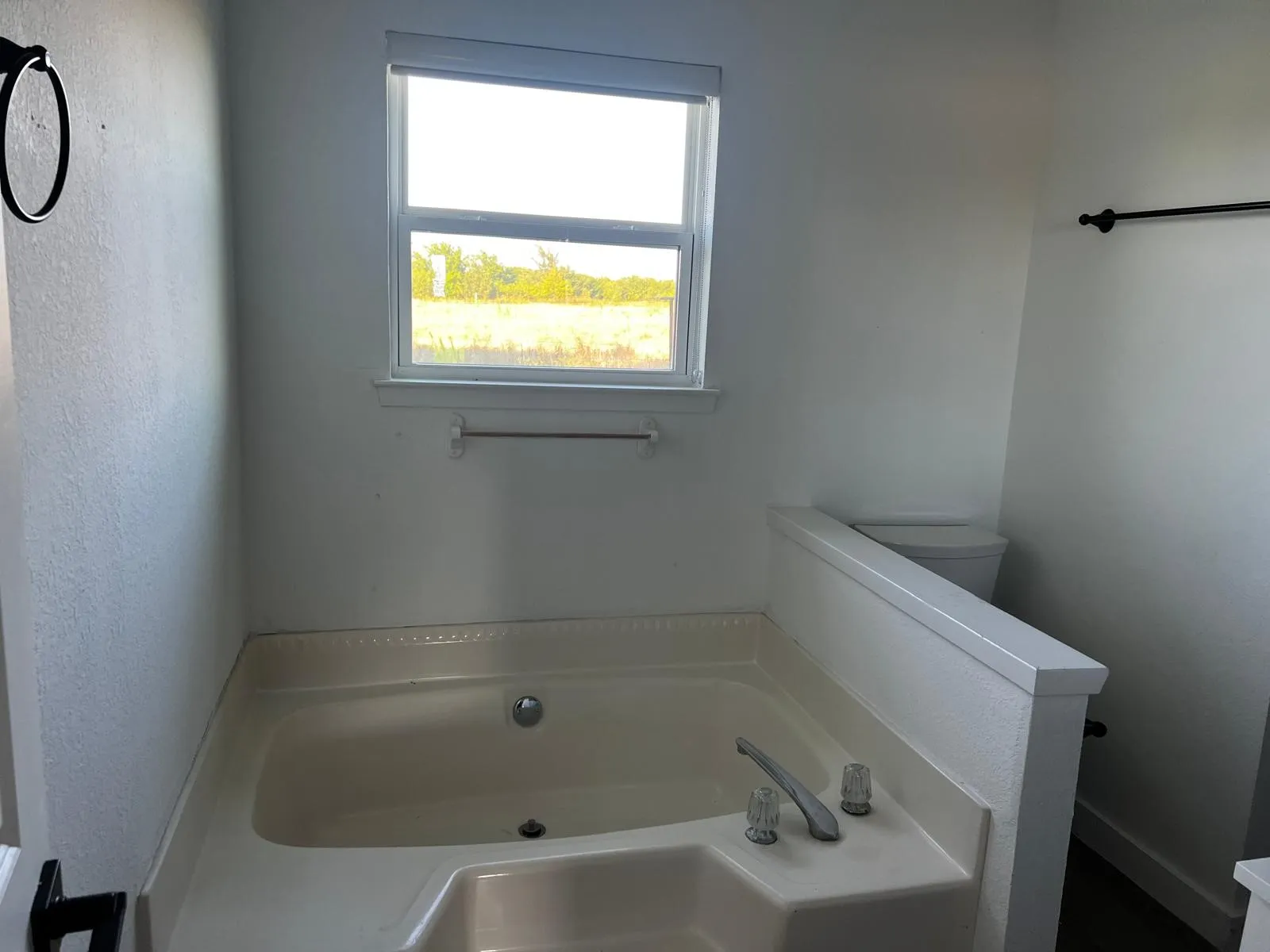 Built-in soaking tub with deck-mounted faucet, privacy wall, and window with blinds