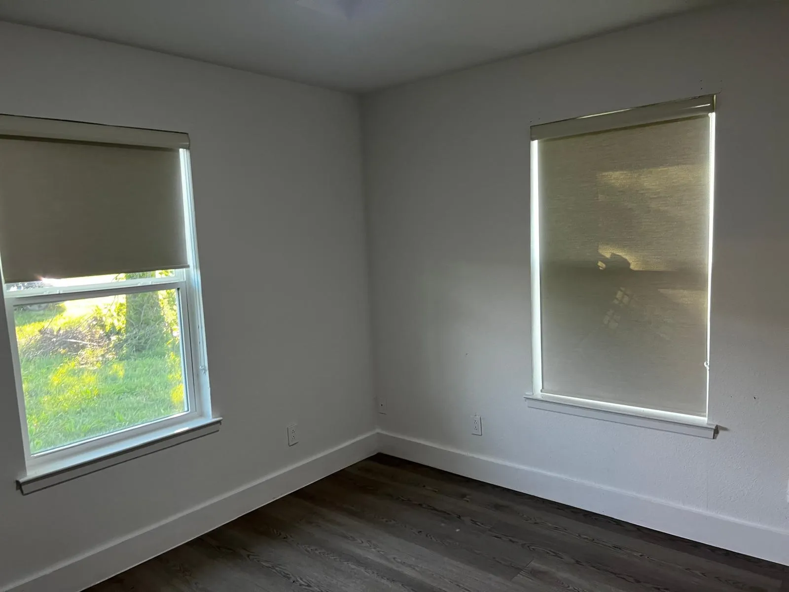 Wood-finish flooring, white walls, and two windows with roller shades