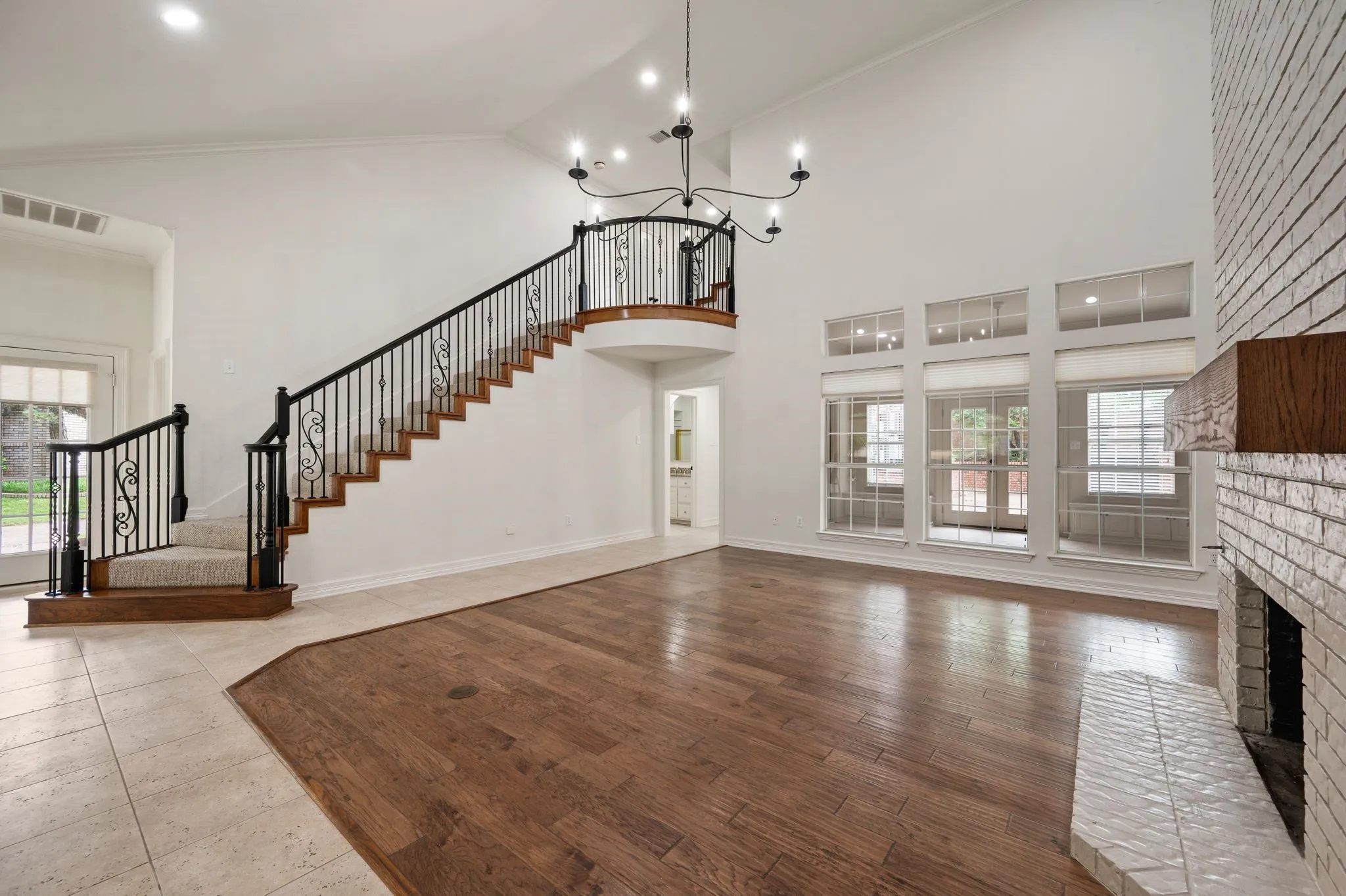 Unfurnished living room with an inviting chandelier, a brick fireplace, high vaulted ceiling, stairs, and visible vents
