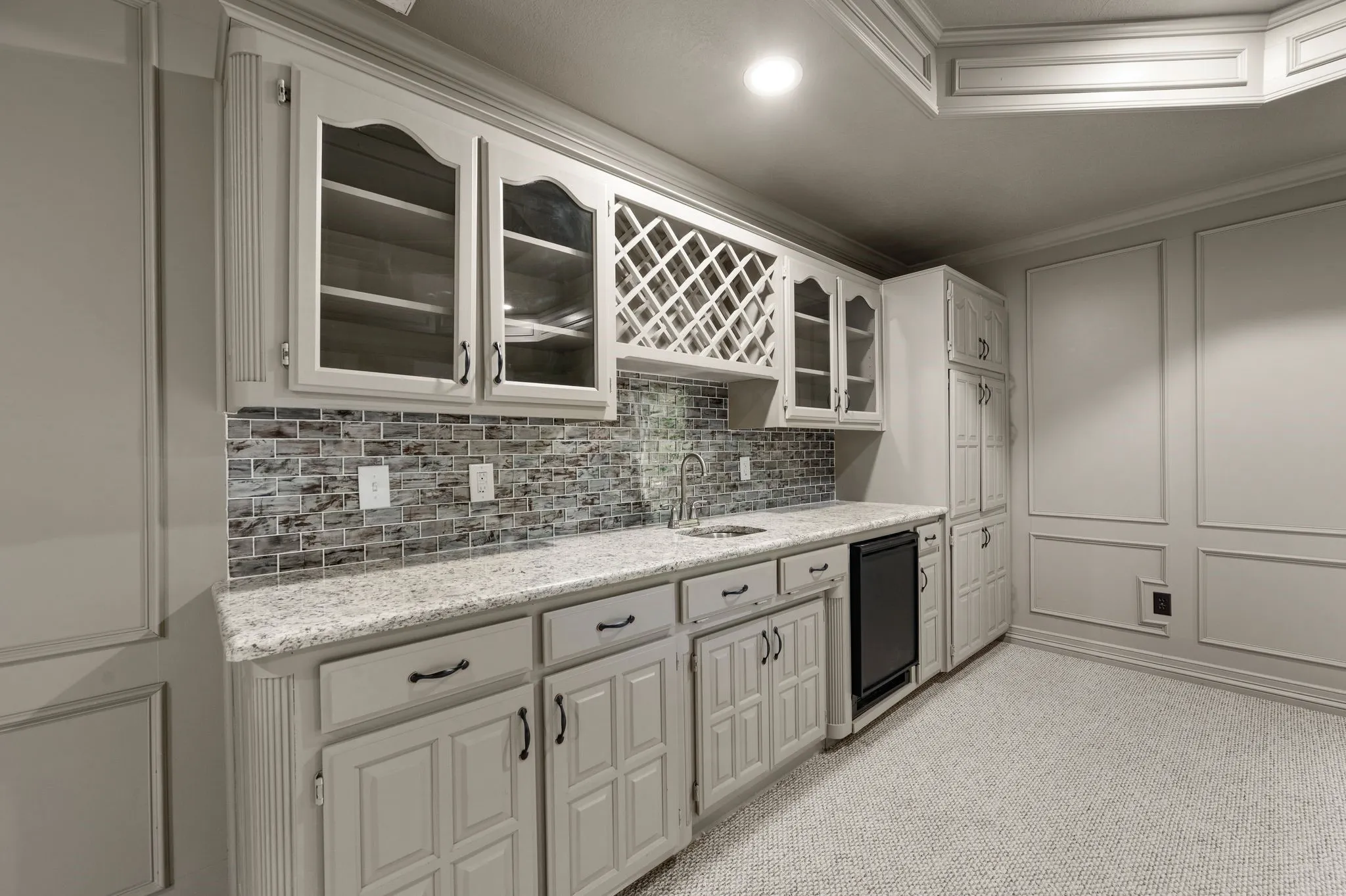 Kitchen featuring a sink, backsplash, light stone countertops, and glass insert cabinets