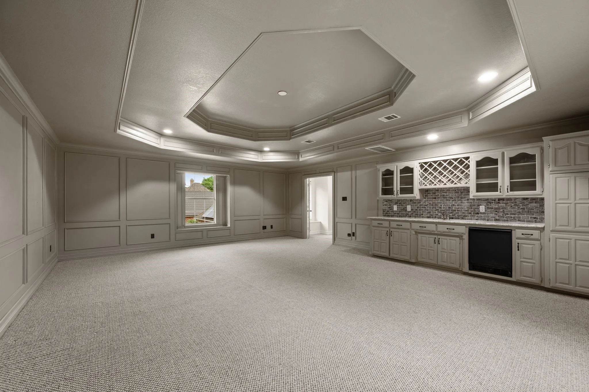 Kitchen with crown molding, light carpet, a decorative wall, a tray ceiling, and glass insert cabinets