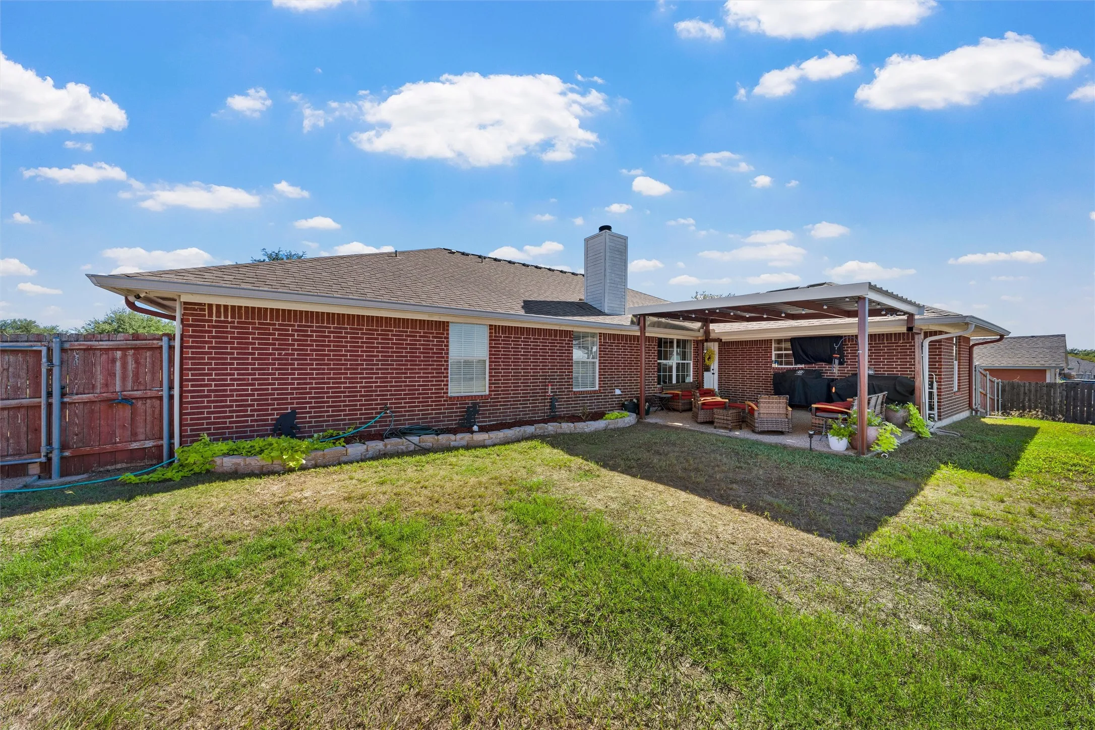 Brick exterior with a covered patio, a privacy fence, and a chimney