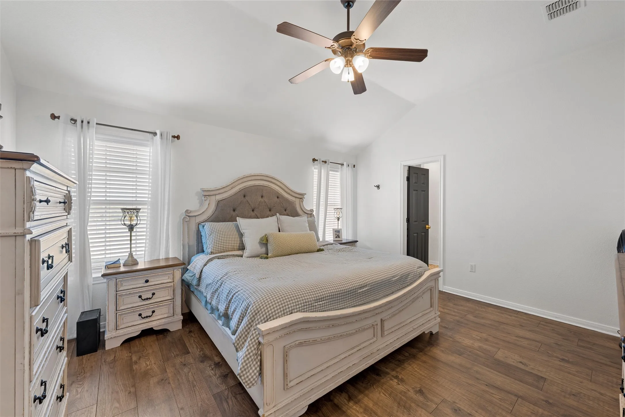 Vaulted ceiling with a ceiling fan, wood-finish flooring, white walls, and a dark paneled door